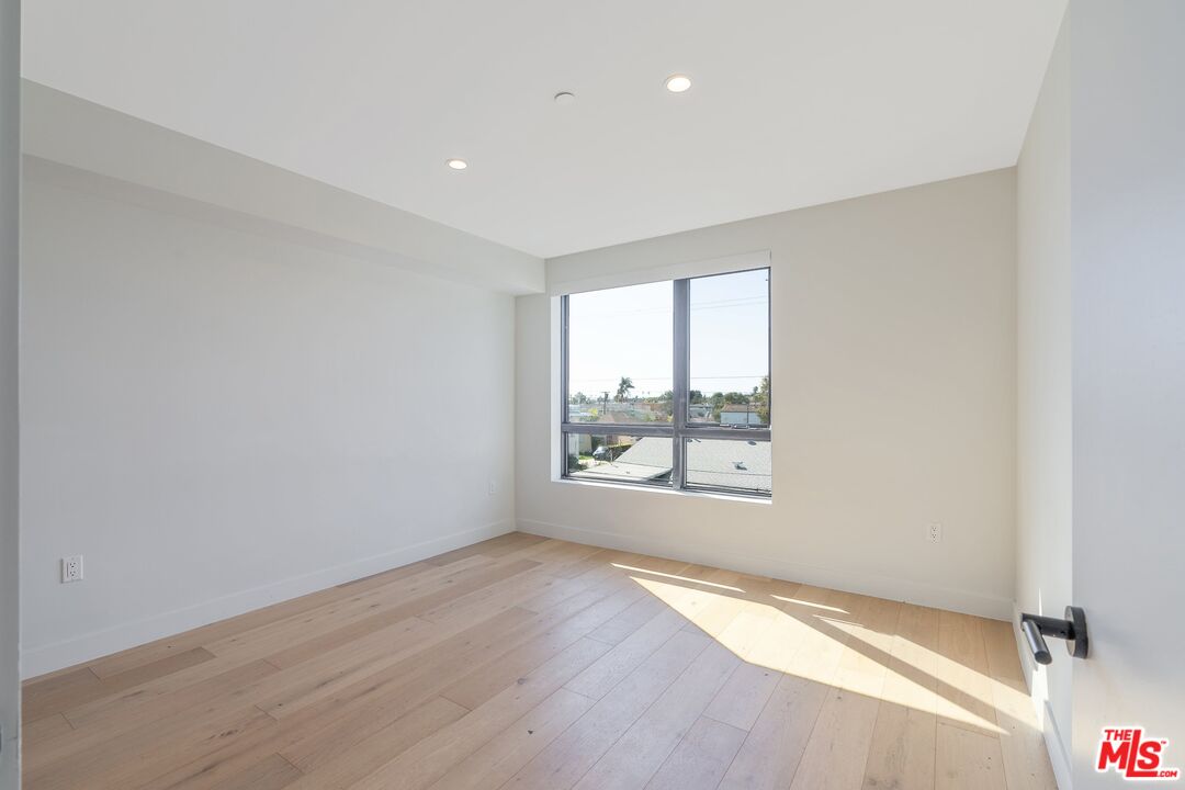 Empty room with light wood flooring and a large window overlooking rooftops.