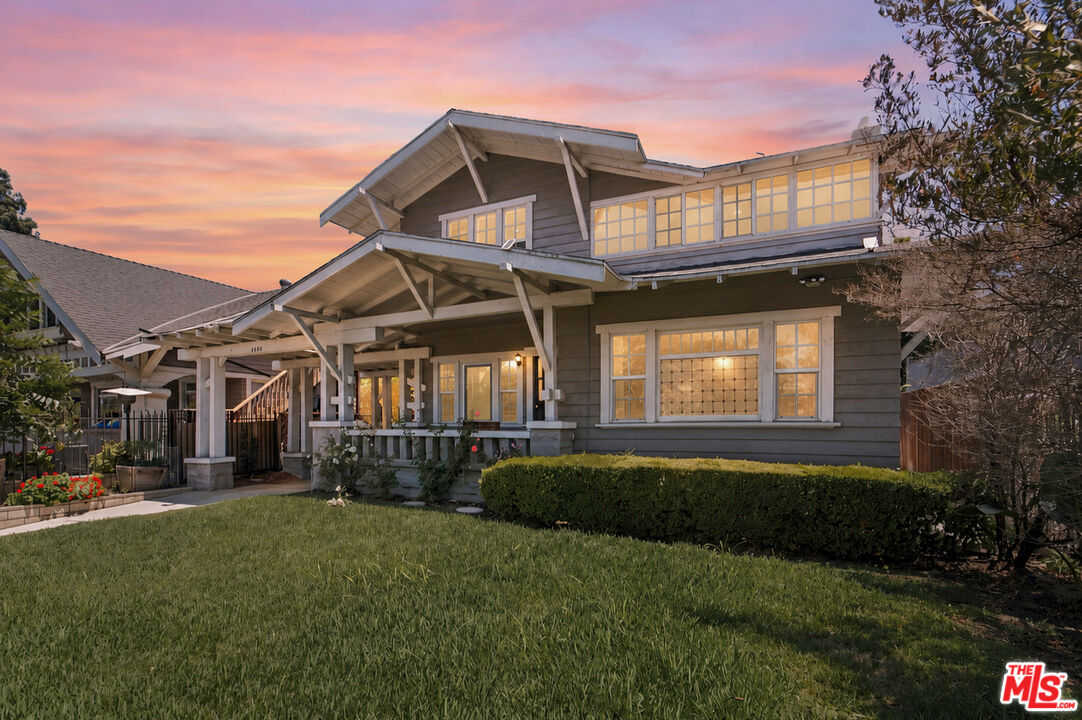 Gray two-story Craftsman house with a broad covered porch and glowing windows at sunset.