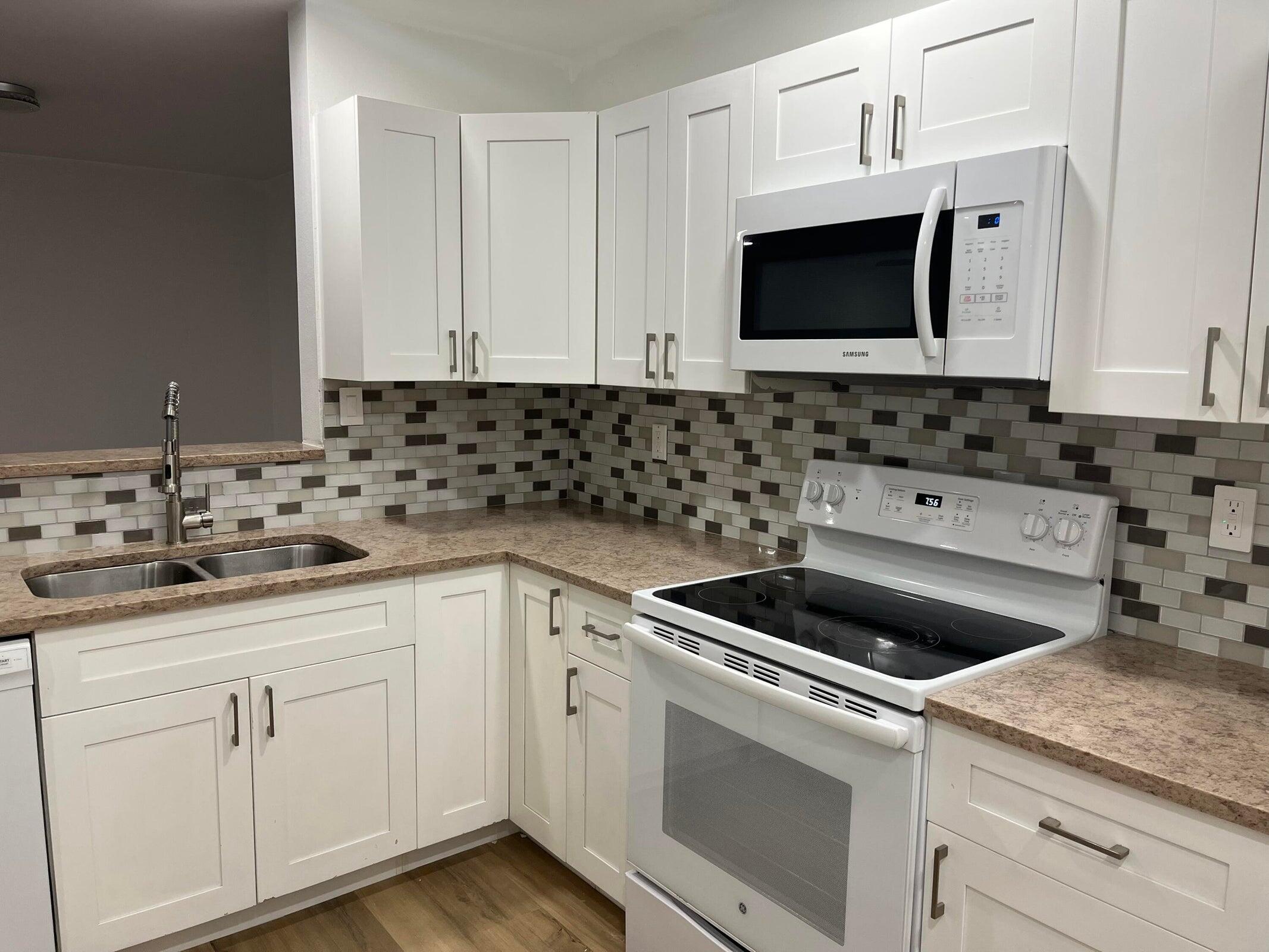 Kitchen with white cabinets, granite counters, patterned tile backsplash, and white electric appliances.