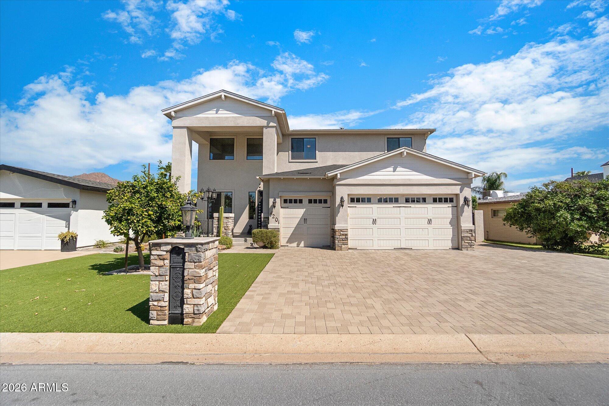 Two-story stucco home with a covered entry, two-car garage, paver driveway, and landscaped front lawn.