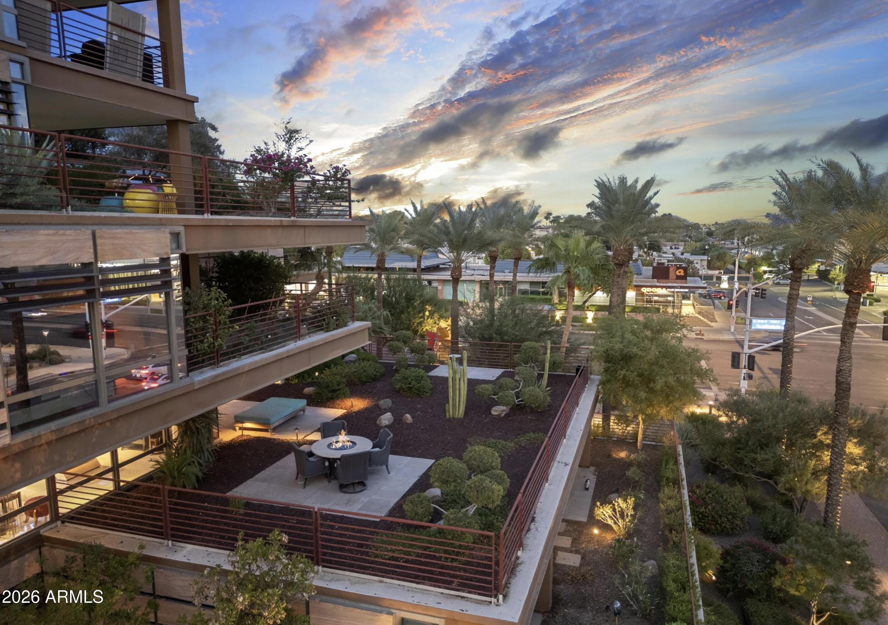 Modern condominium terrace with a fire pit, landscaped courtyard, palm trees, and downtown views at dusk.