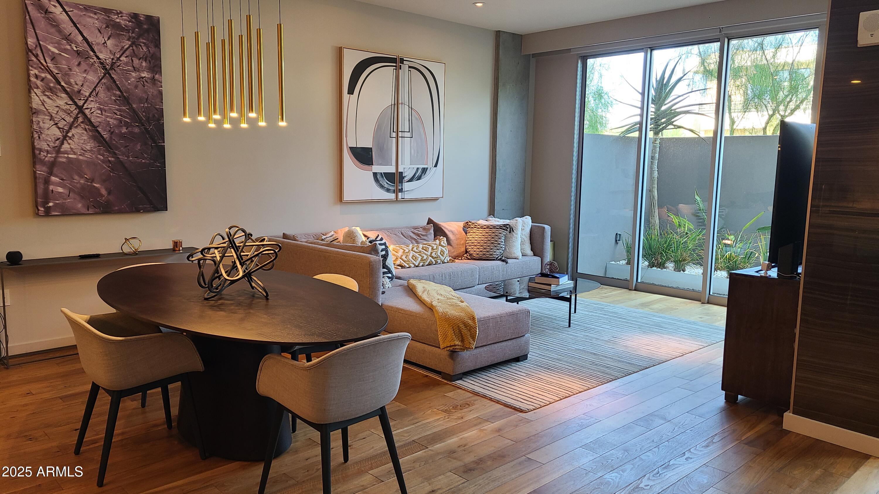 Furnished condo living and dining area with a sectional sofa and sliding glass doors to a landscaped patio.