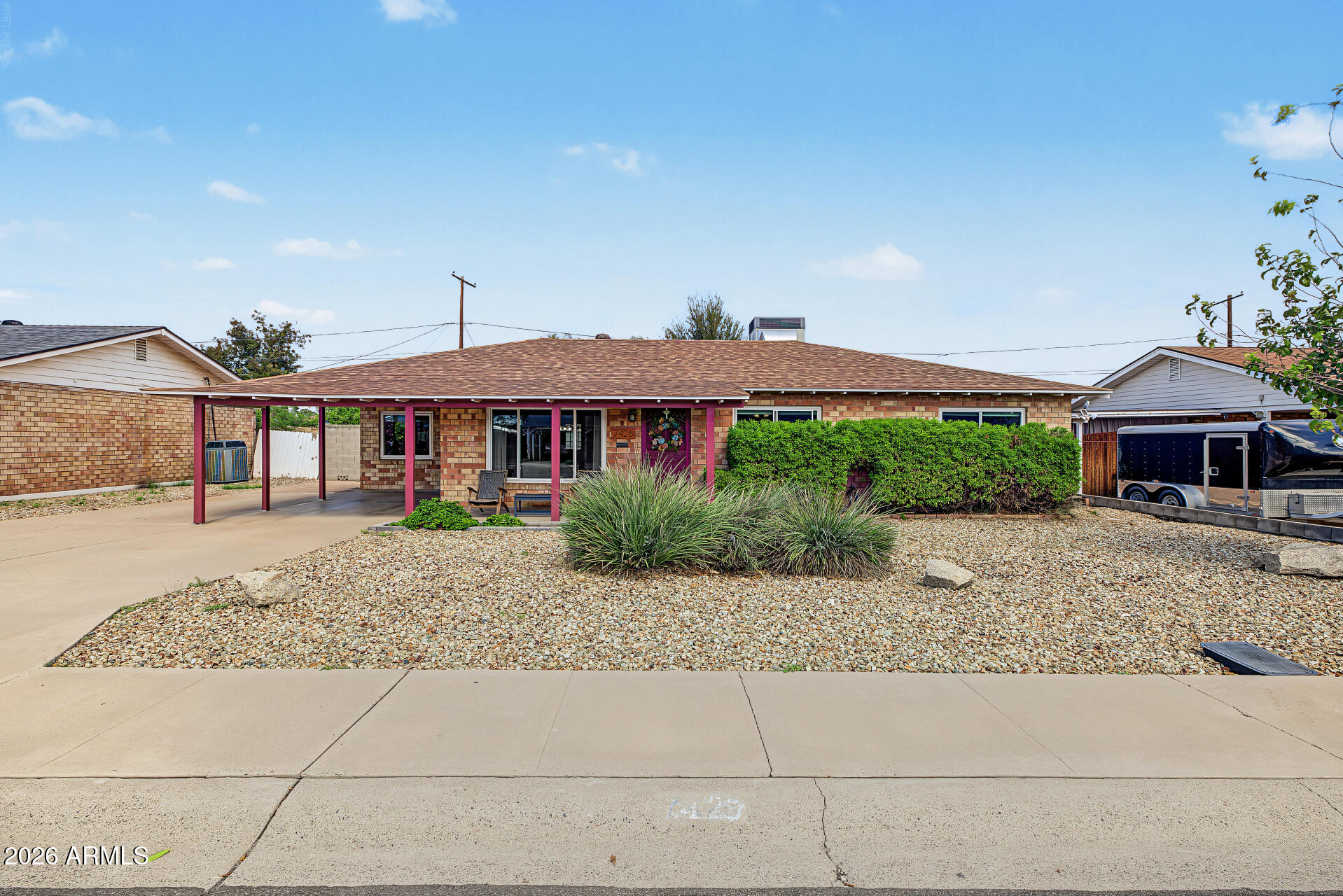 Single-story brick home with a covered carport, front patio, and gravel desert landscaping.