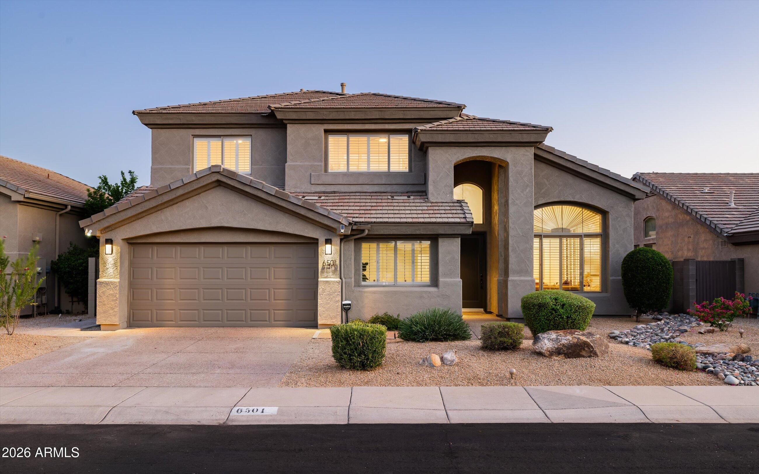 Two-story stucco home with a tile roof, two-car garage, and desert landscaping at dusk.