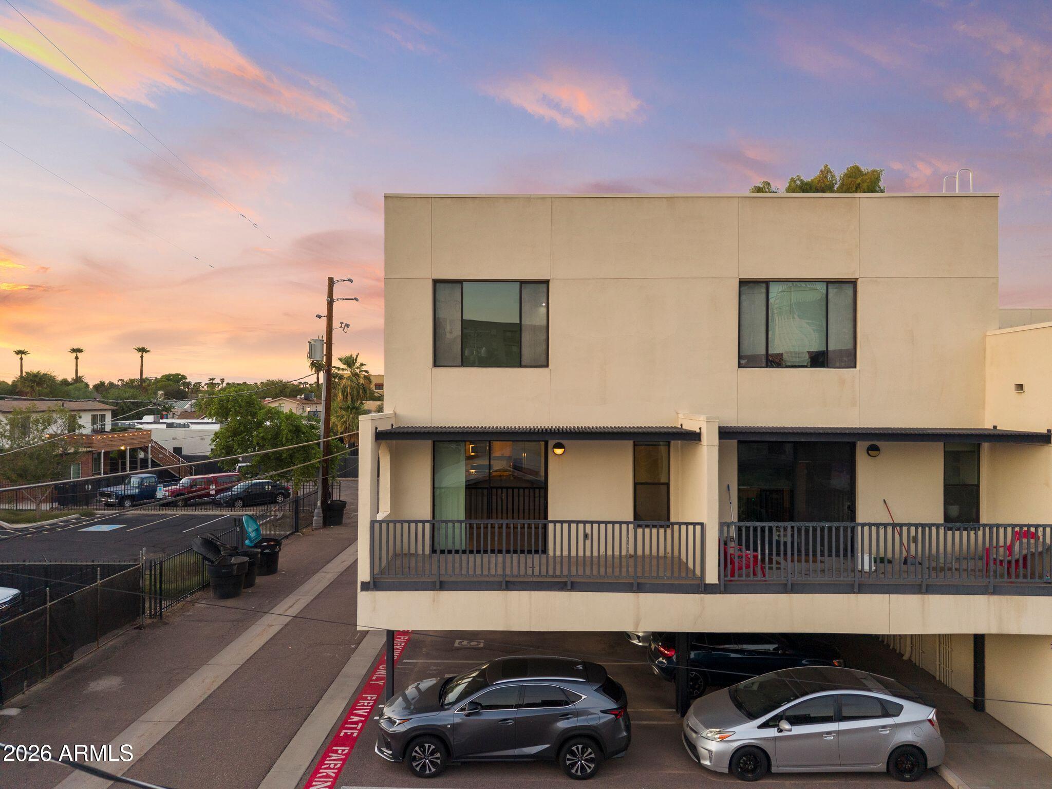 Modern beige residential building with balconies and covered parking at dusk.