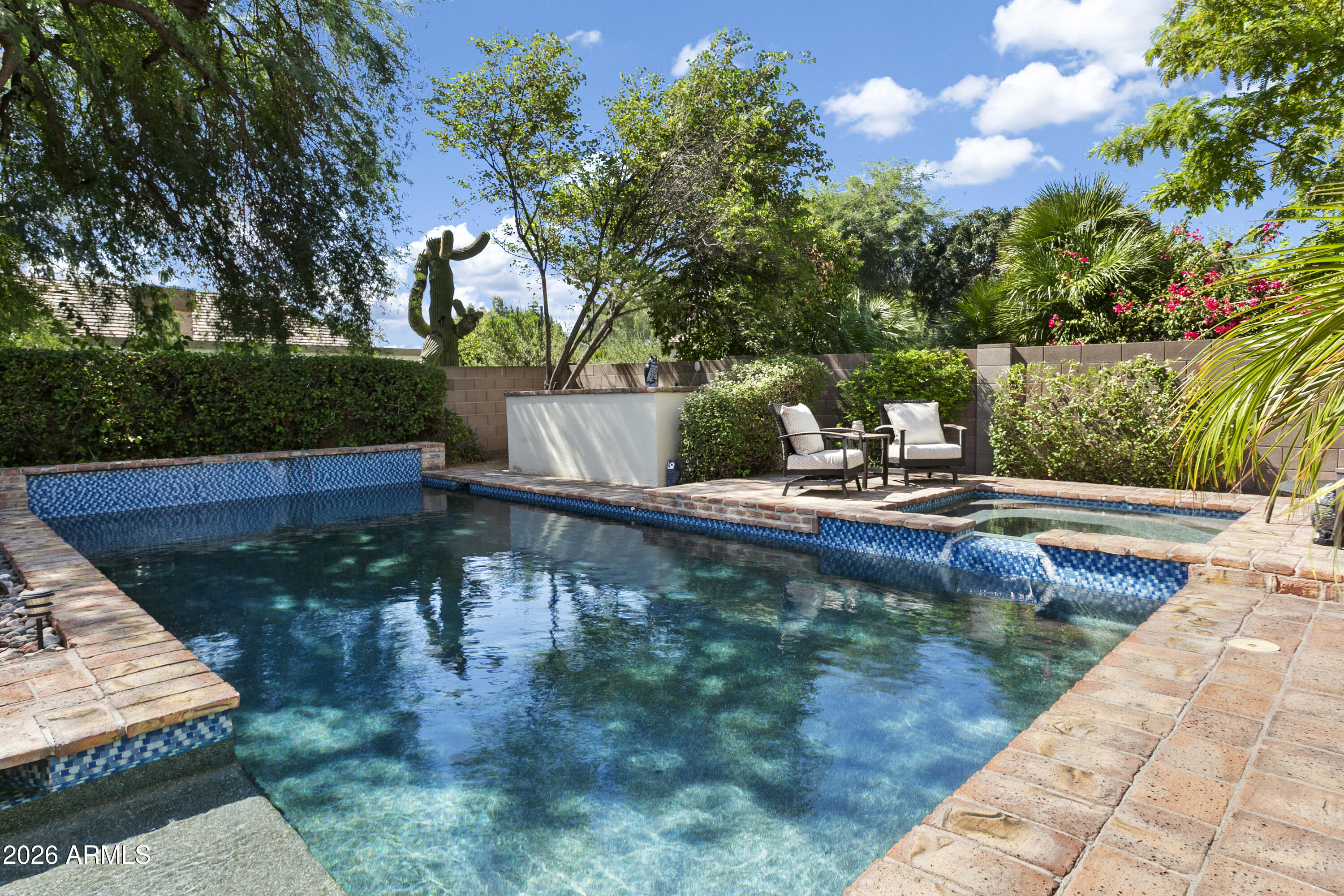 Backyard swimming pool with blue tile, brick coping, raised spa, and patio seating.