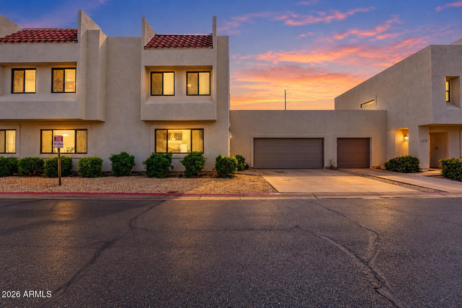 Stucco townhouse exterior with tiled roofs and two garages beneath a vivid sunset sky.