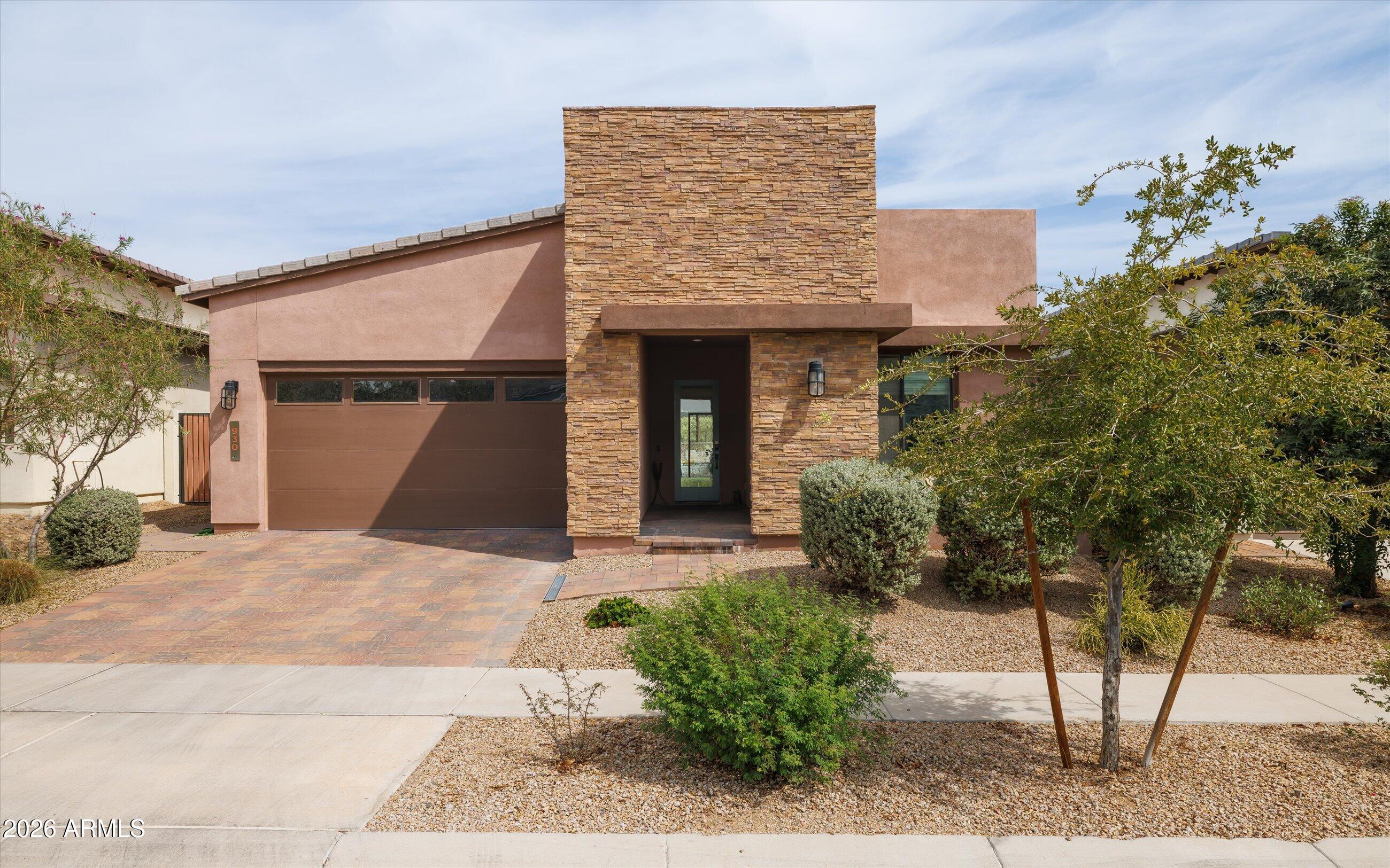 Modern home with a tall stone entry feature, paver driveway, and desert landscaping.
