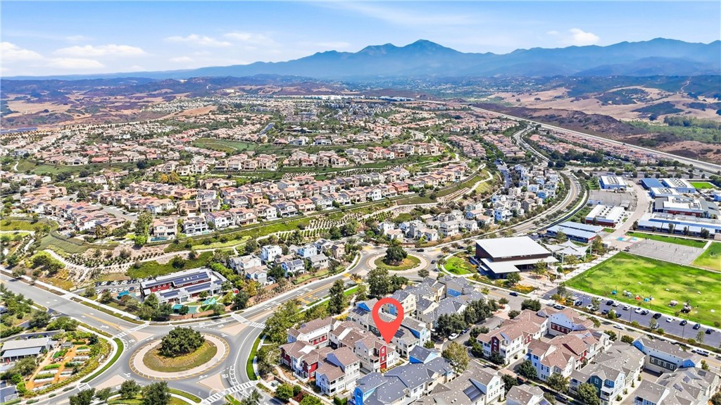 Aerial neighborhood view with a red pin marking a home, roads, sports fields, and distant mountains.
