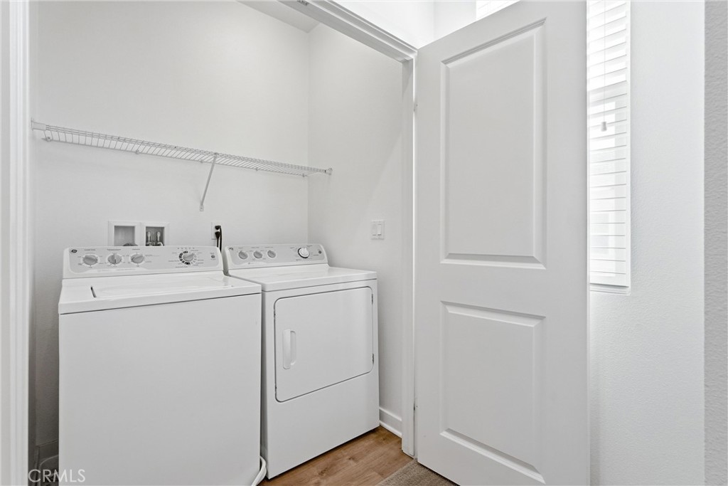 Laundry room with a white washer and dryer beneath a wire shelf.