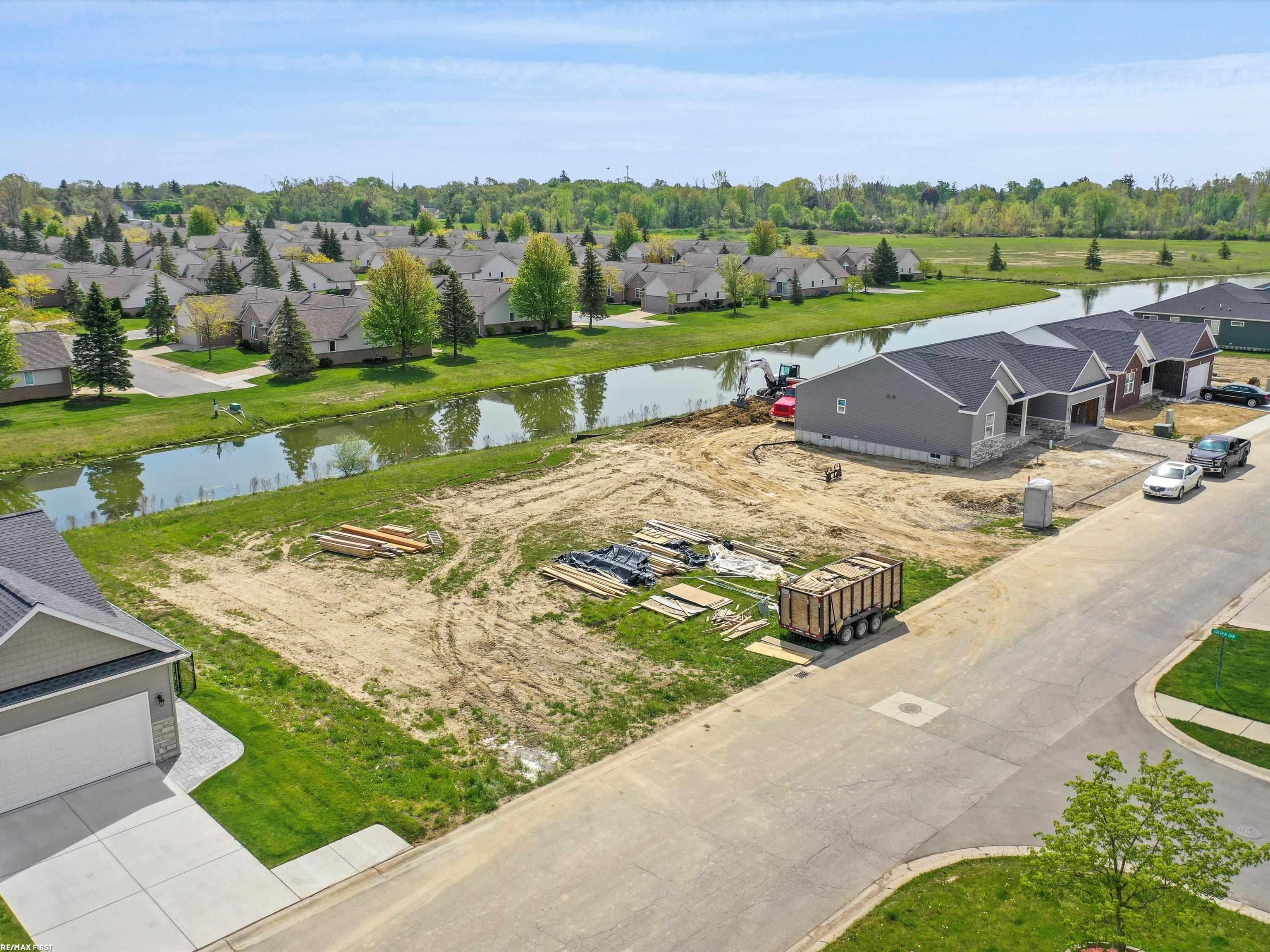 Home under construction beside a waterway, surrounded by neighboring houses and a residential street.