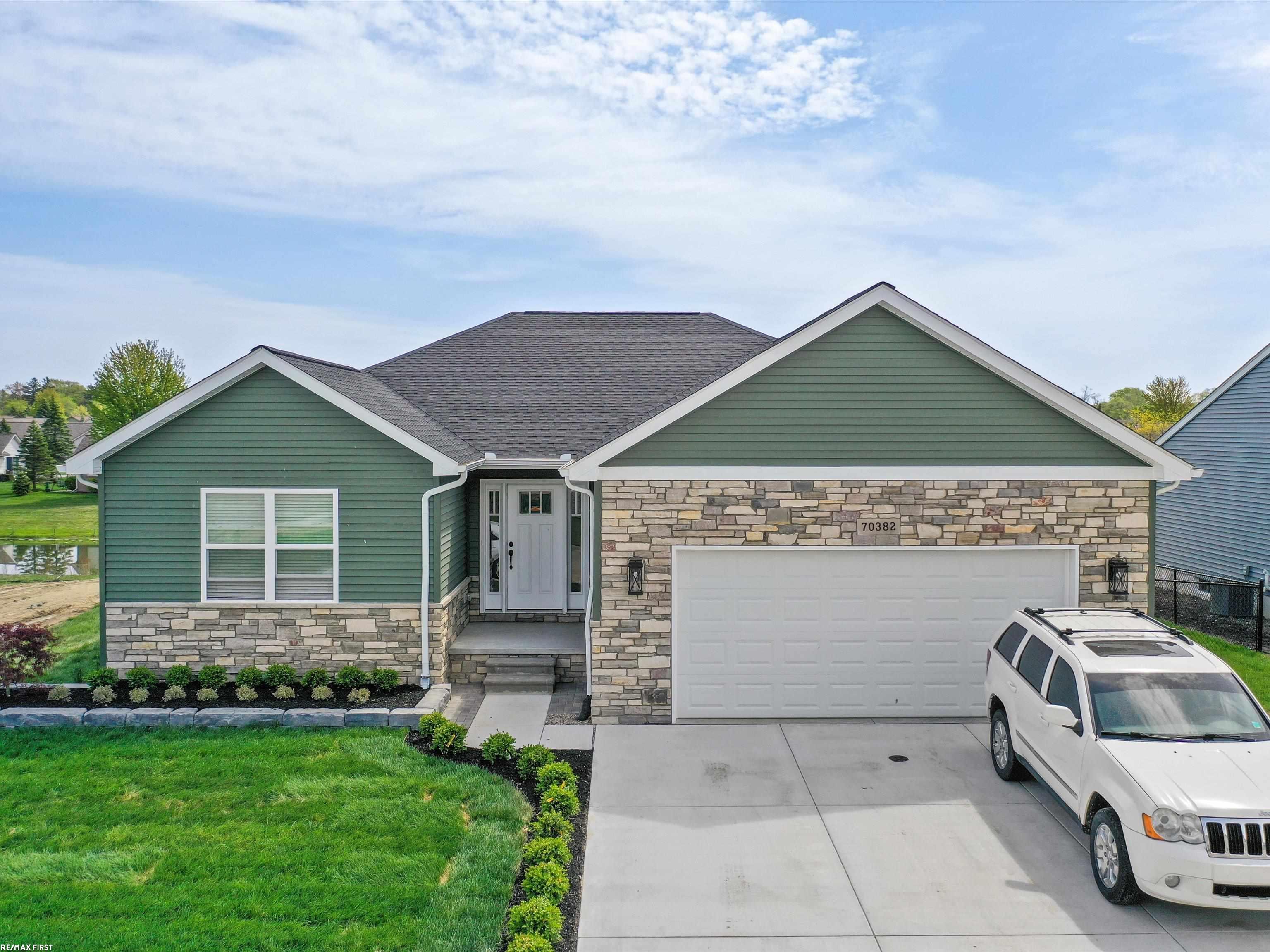Green-sided home with stone facade and two-car garage, viewed from the front with a white SUV in the driveway.
