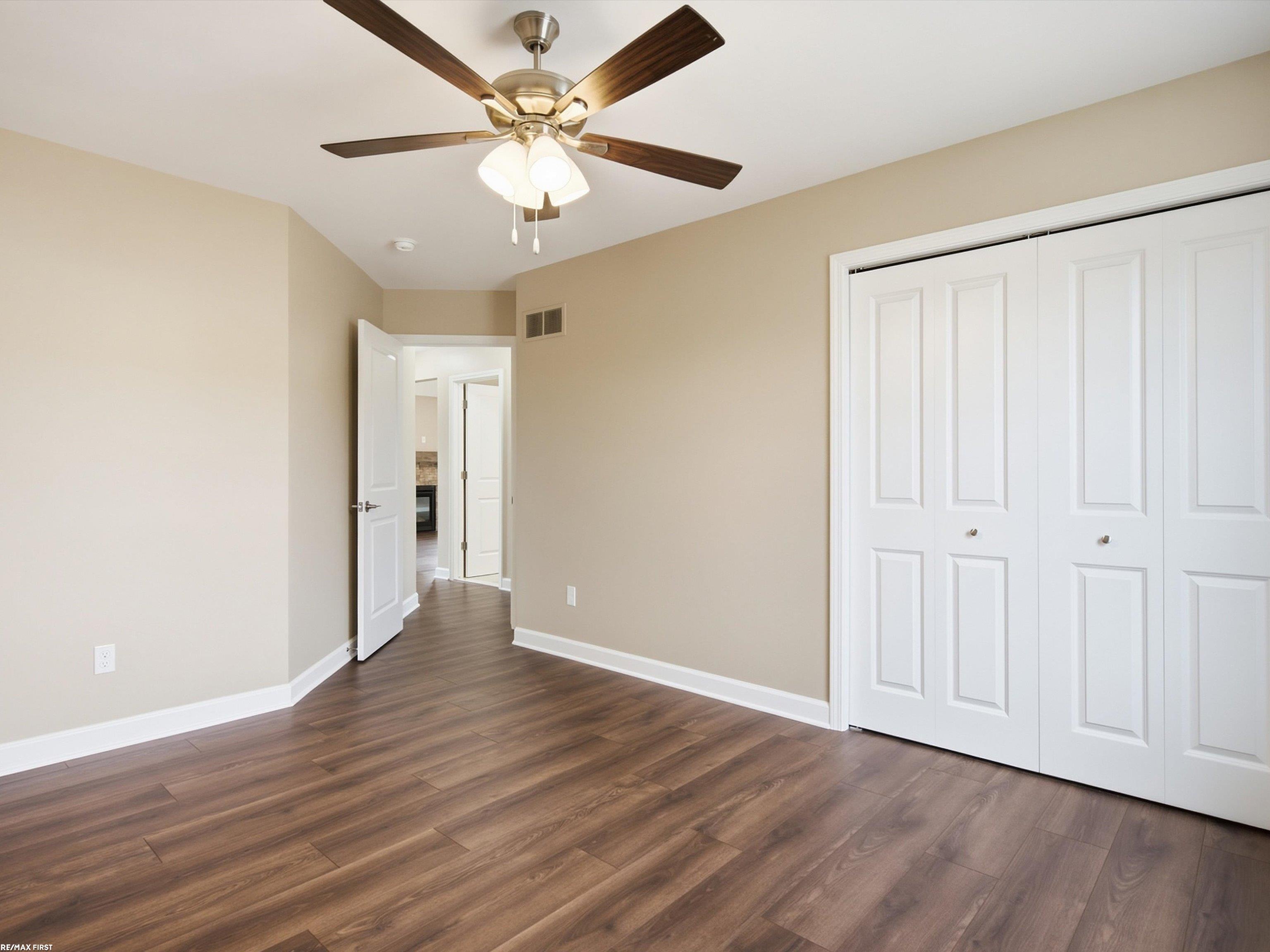 Empty bedroom with dark wood-look floors, white closet doors, and a ceiling fan.