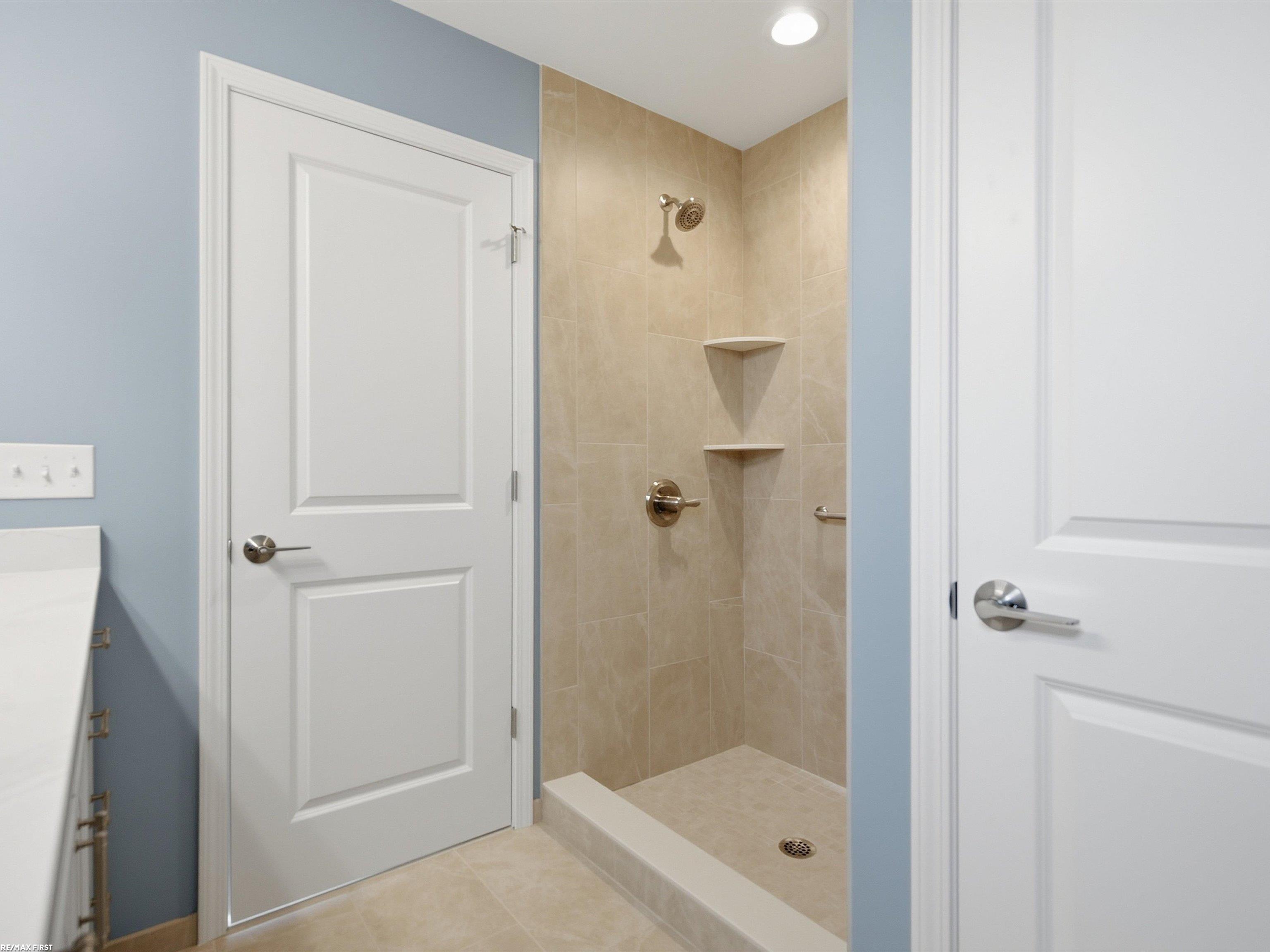 Bathroom walk-in shower with beige tile, built-in corner shelves, and chrome fixtures.
