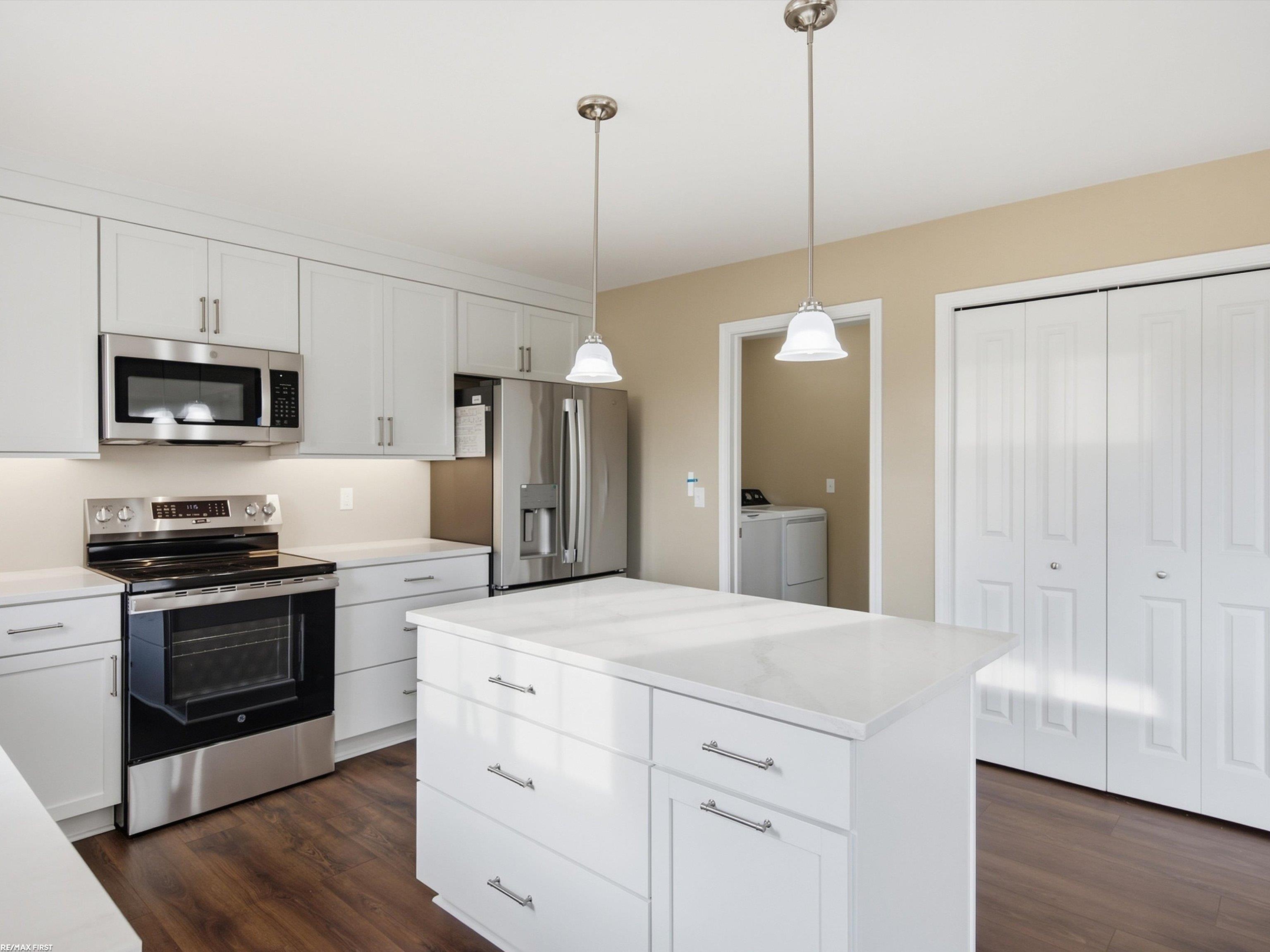 Modern white kitchen with a large island, stainless steel appliances, and laundry area beyond the doorway.