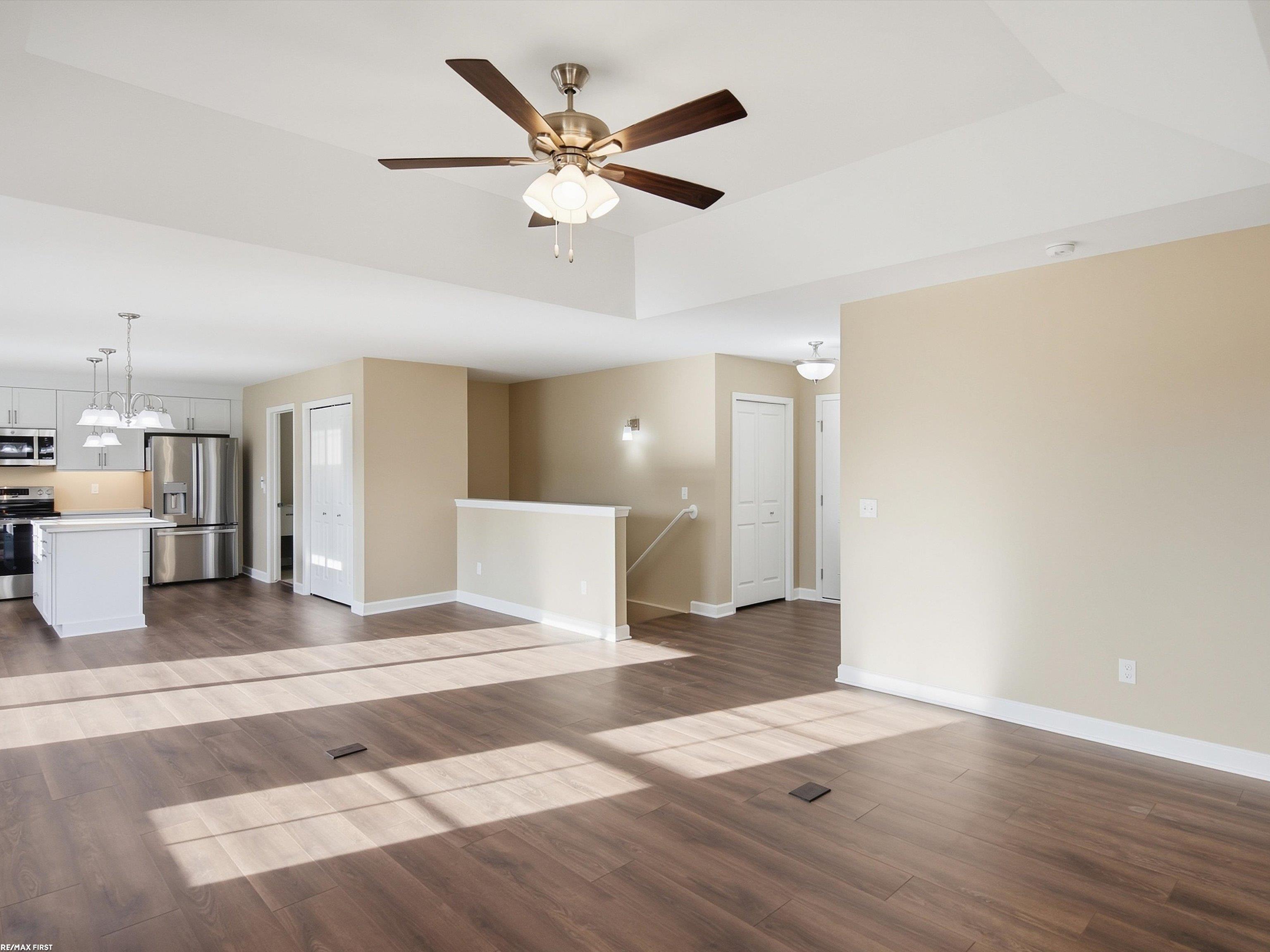 Vacant open-plan living area with dark flooring, ceiling fan, and adjoining kitchen with island.