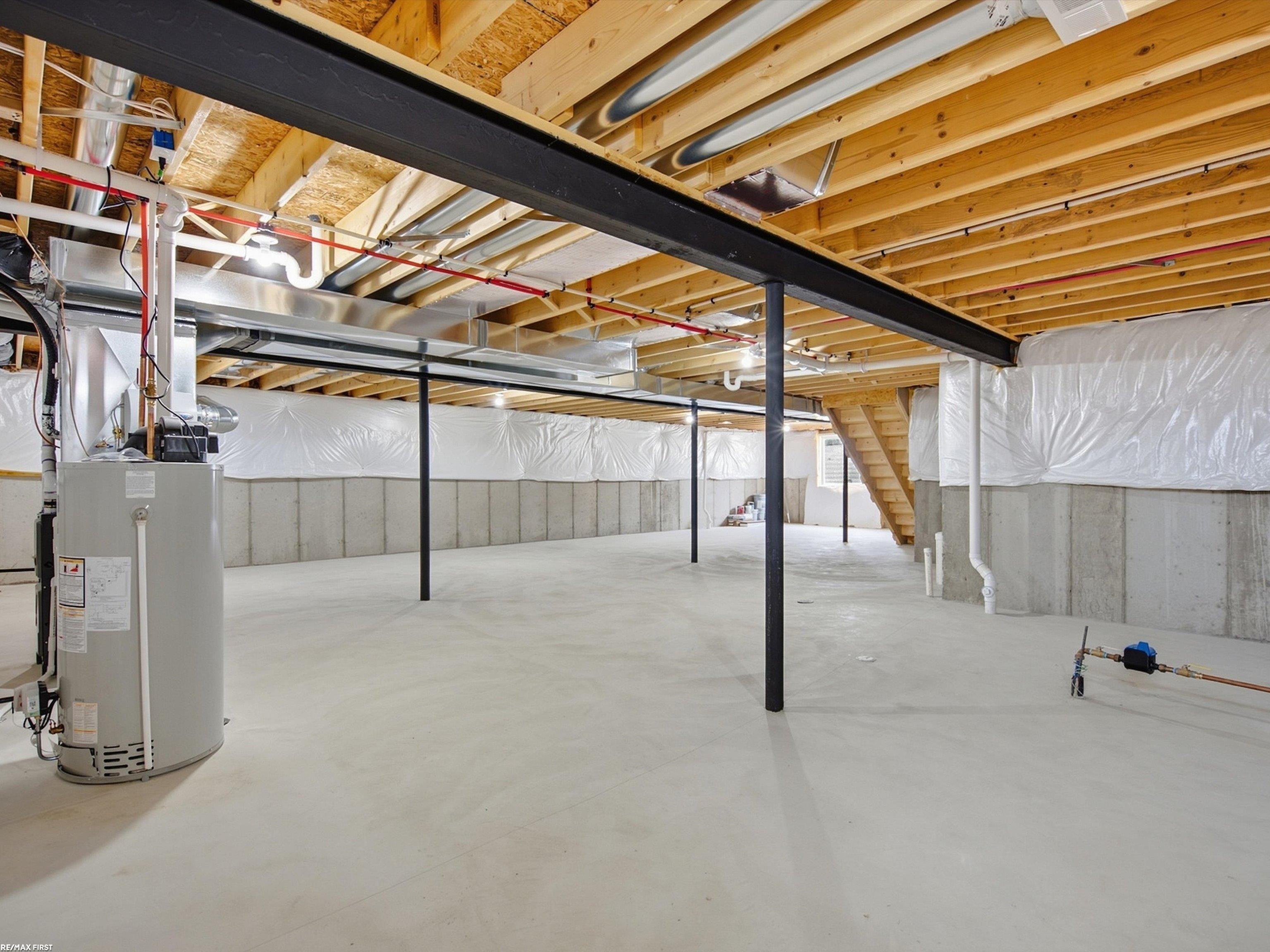 Unfinished basement with exposed wood joists, black support posts, and a water heater.