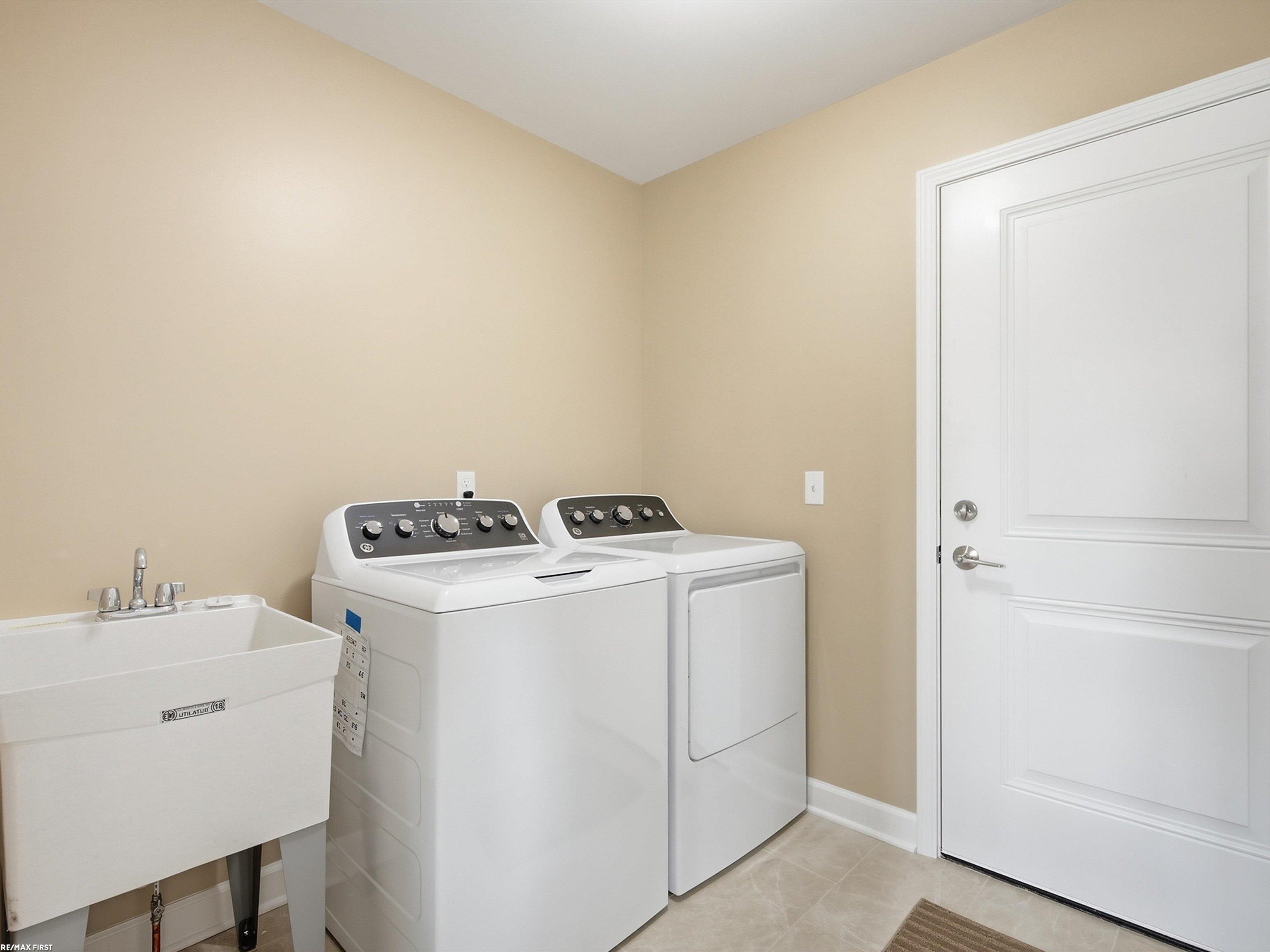 Laundry room with a washer, dryer, utility sink, and white paneled door.