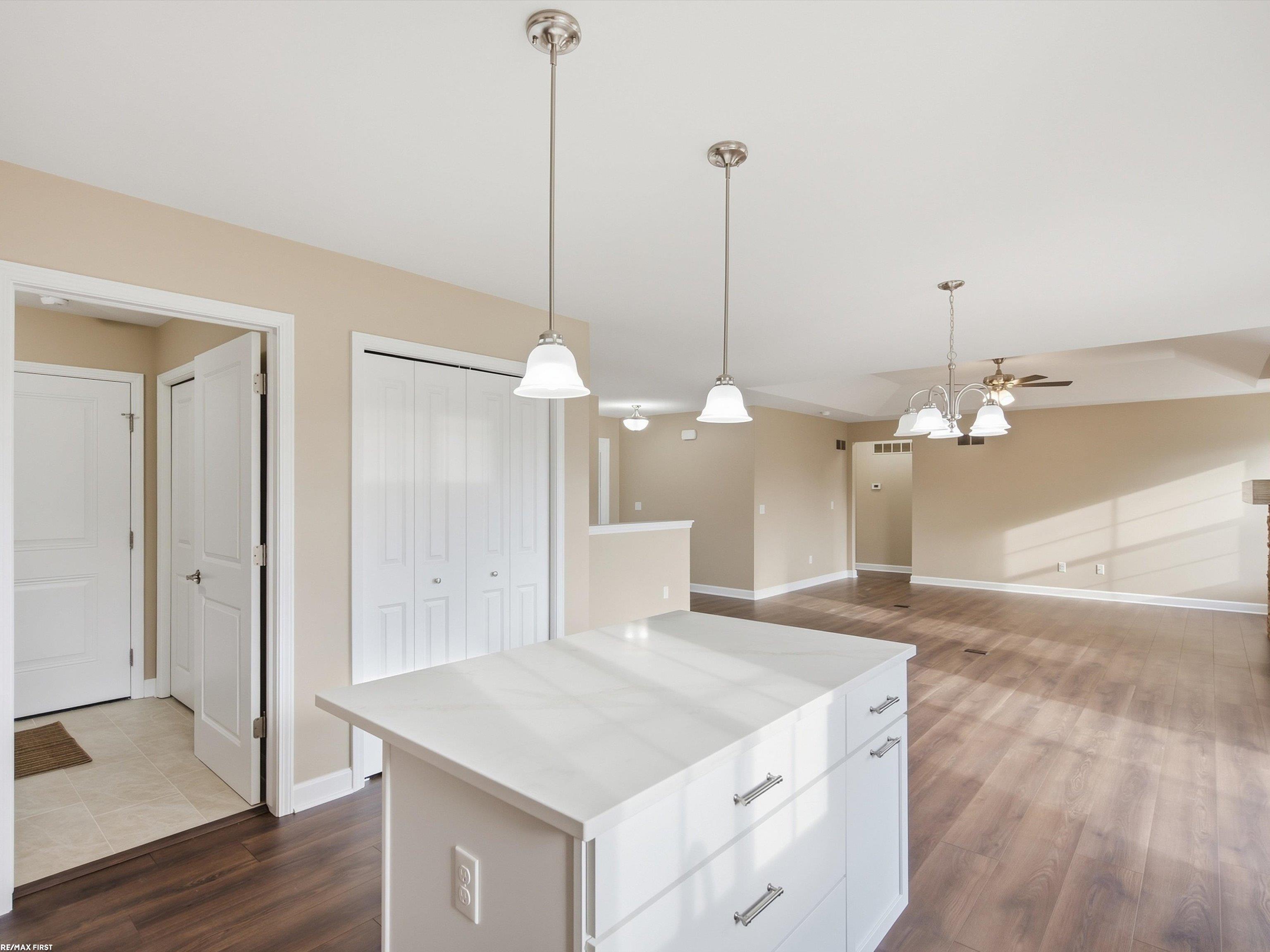 Vacant kitchen with a large white island opening onto a sunlit open-plan living and dining area.