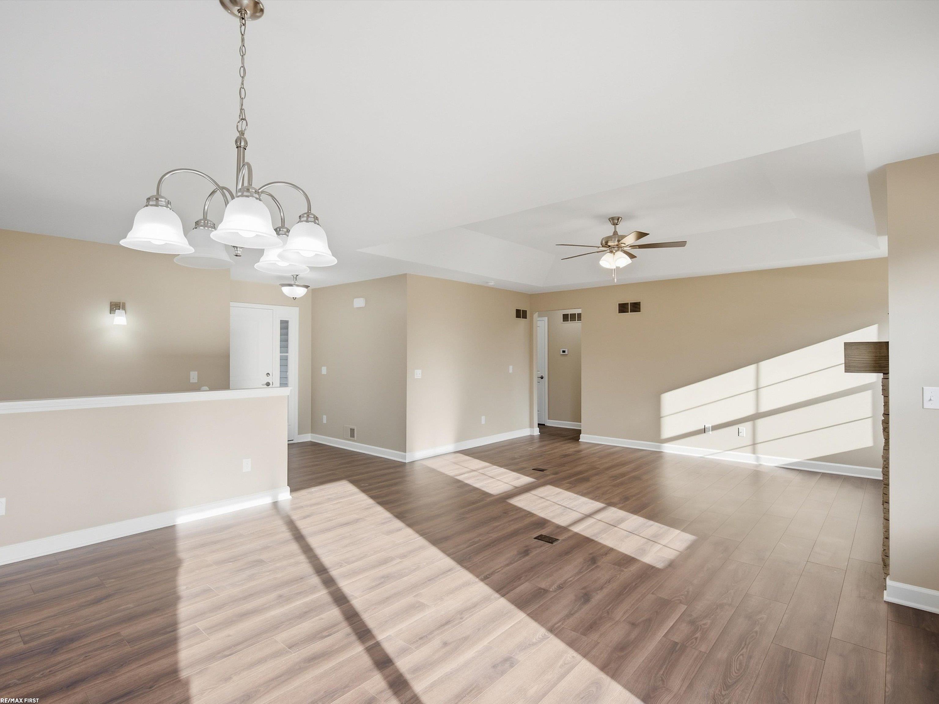 Vacant open-plan living area with wood-look flooring, two ceiling fans, and strong sunlight across the floor.