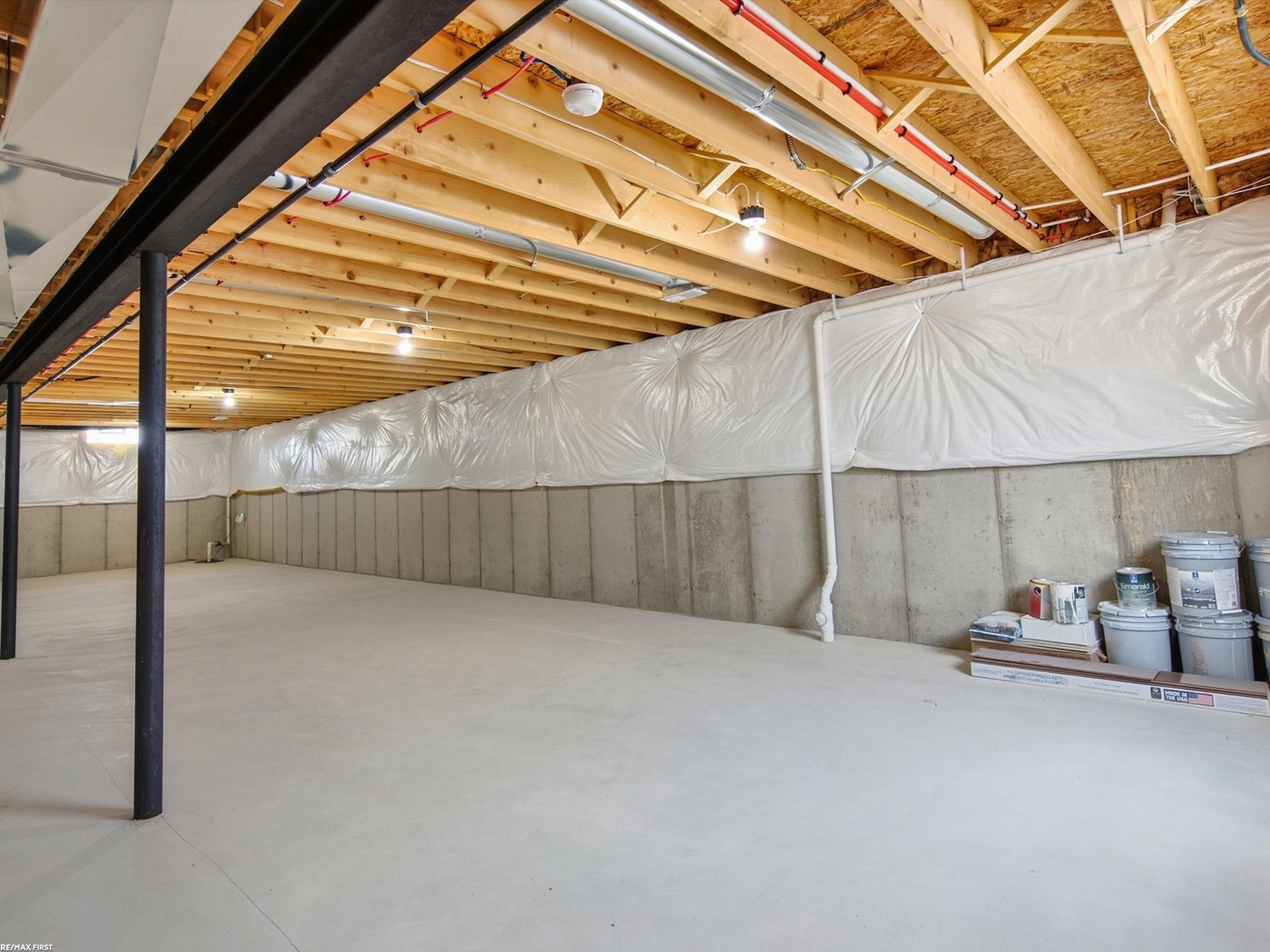 Unfinished basement with exposed ceiling joists, a black support post, and plastic-covered walls.