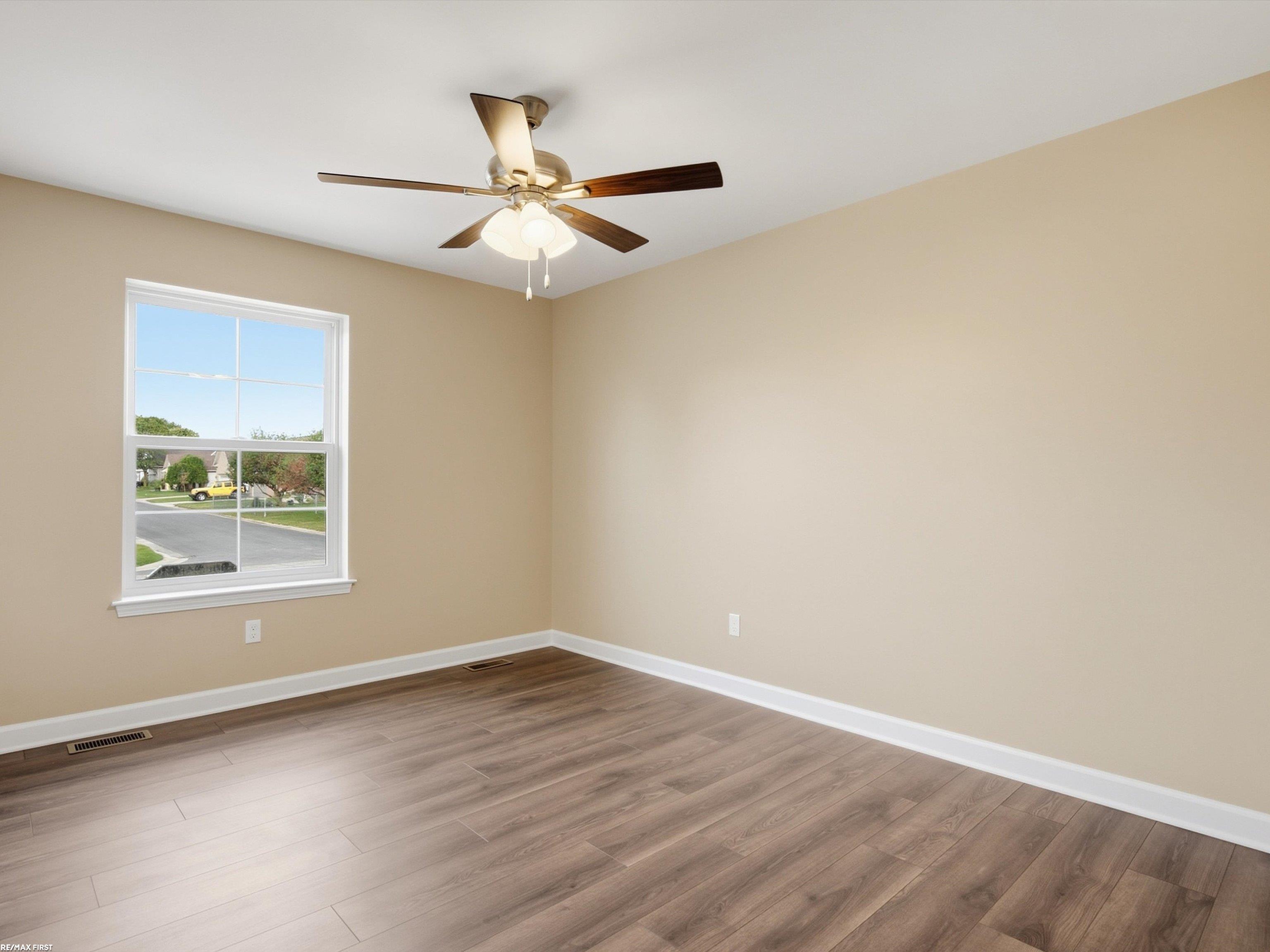 Empty room with beige walls, plank flooring, a ceiling fan, and a street-facing window.