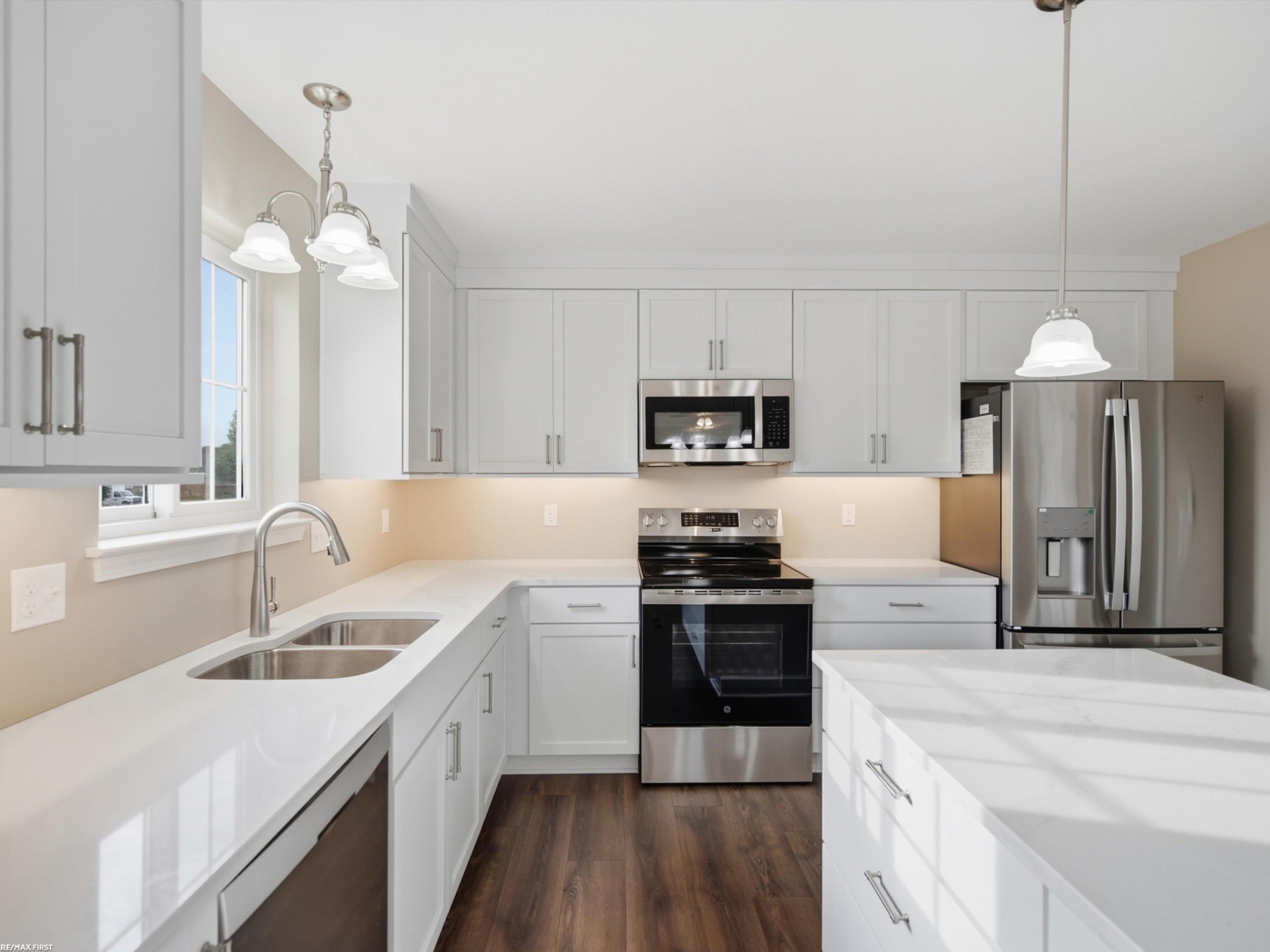 Modern white kitchen with stainless steel appliances, a large island, and dark wood flooring.