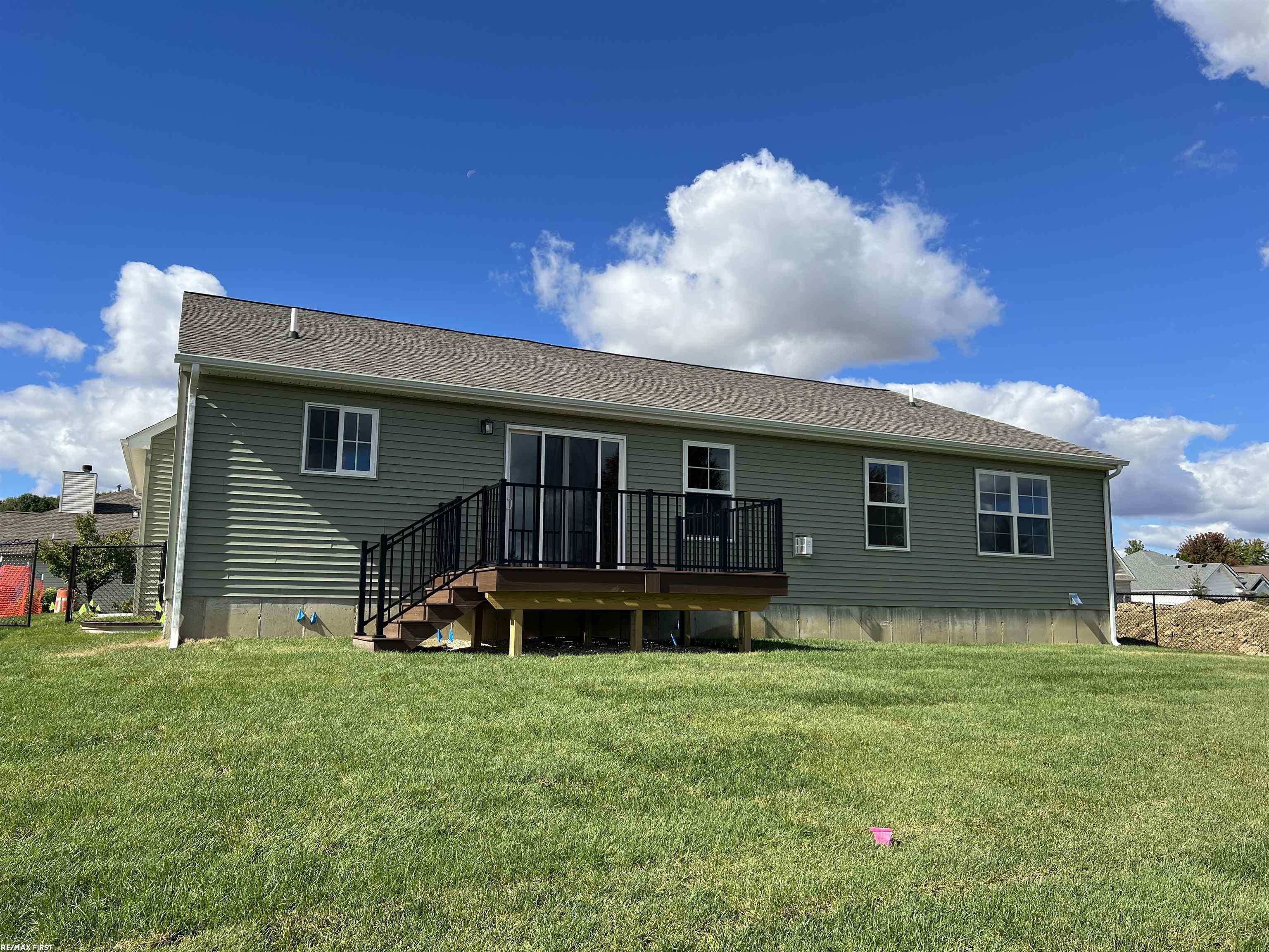 Gray-sided house with a raised deck and black railings overlooking a broad lawn.
