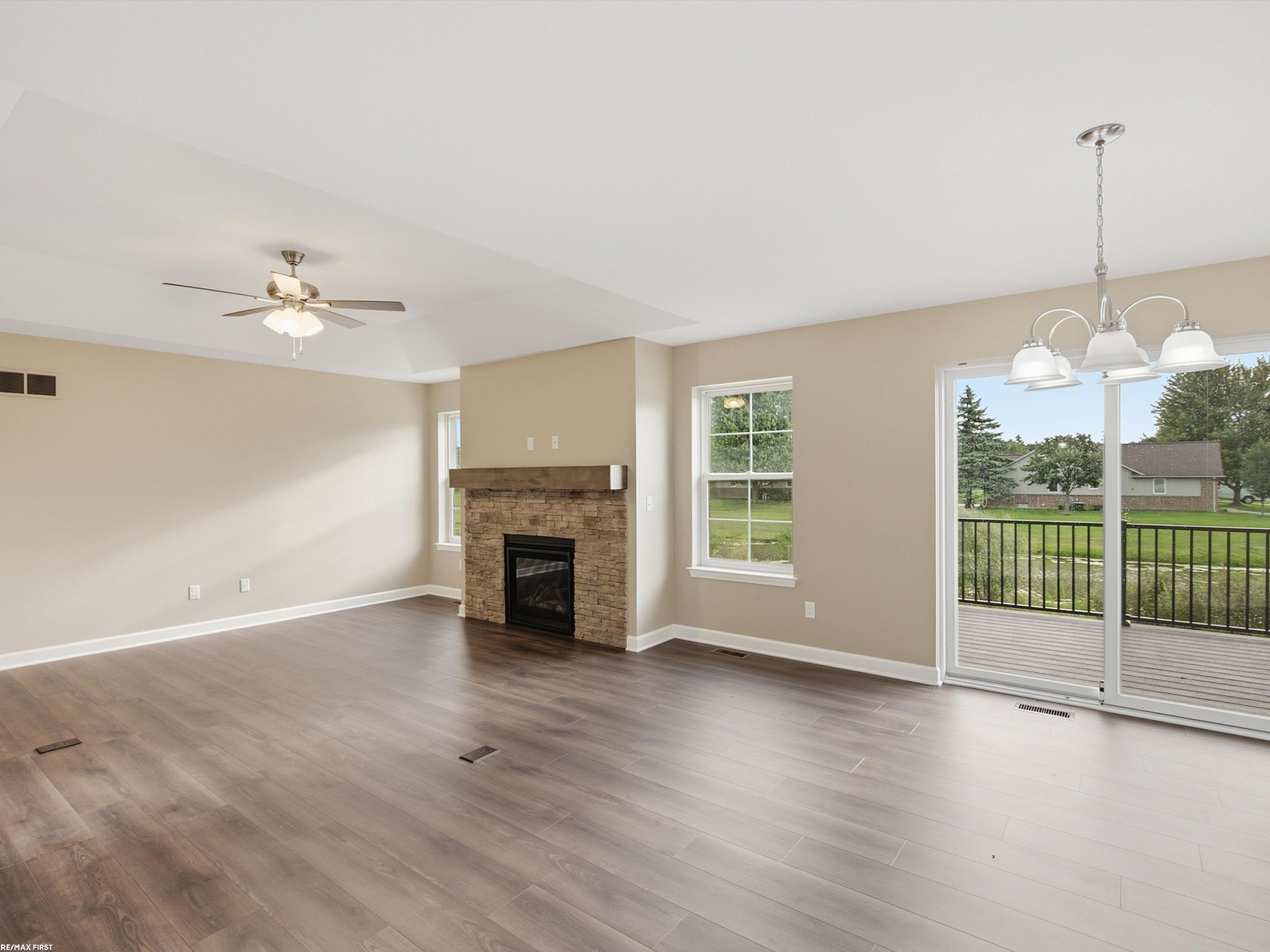 Vacant living room with a stone fireplace, plank flooring, and sliding doors opening to a deck.