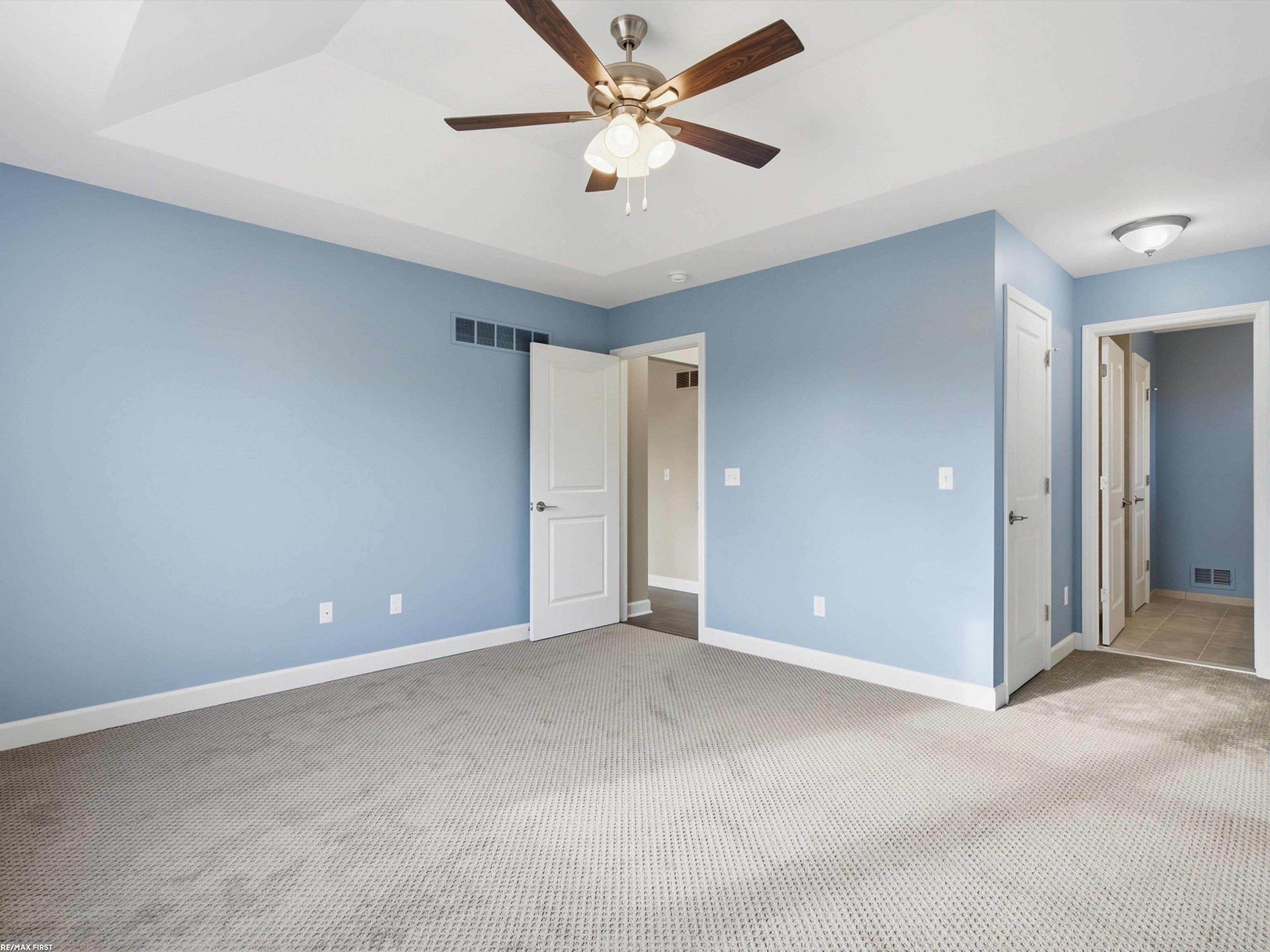 Empty bedroom with blue walls, gray carpet, and a wood-blade ceiling fan.