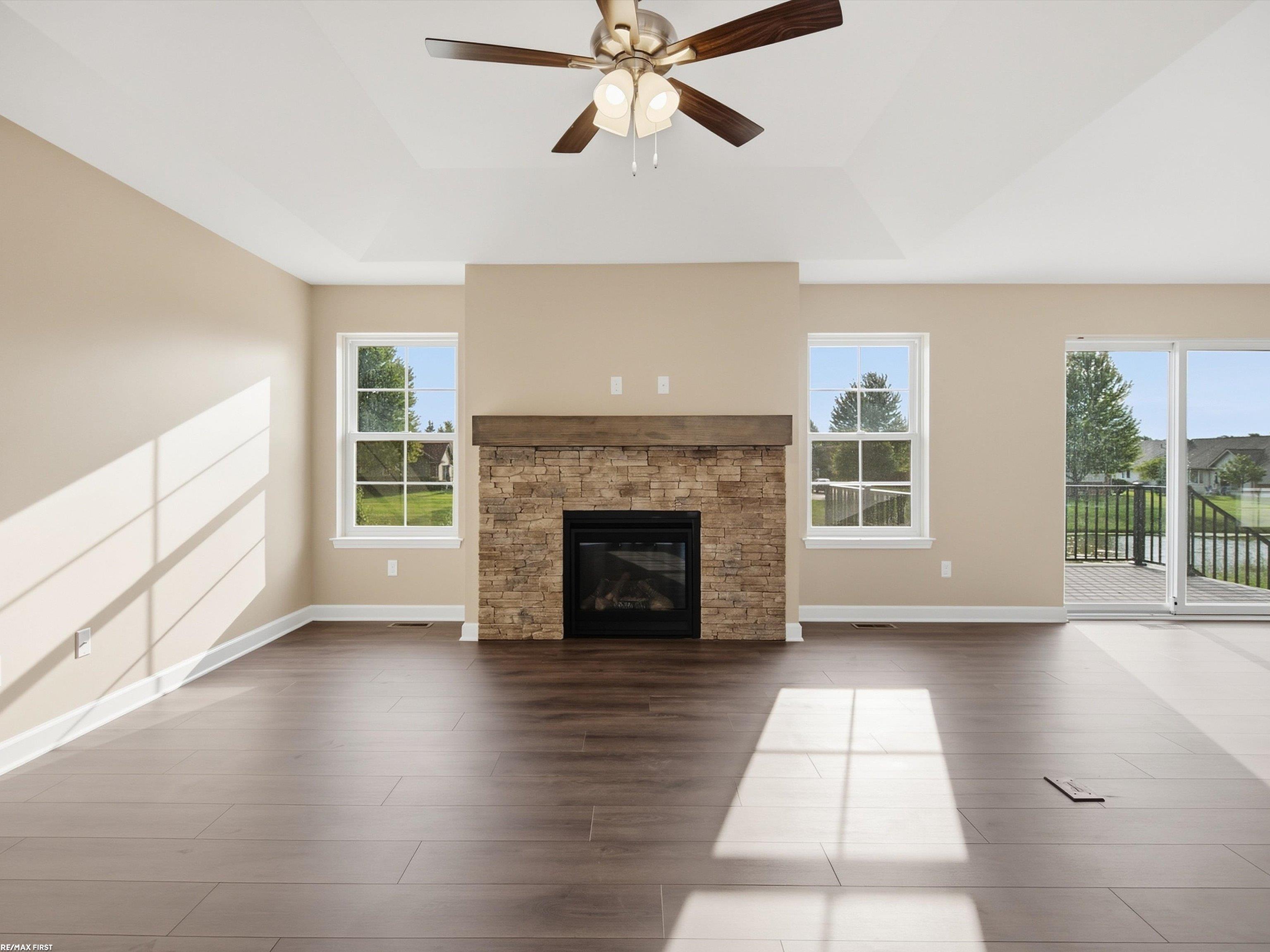 Living room with a stone fireplace, ceiling fan, and sliding doors overlooking water.