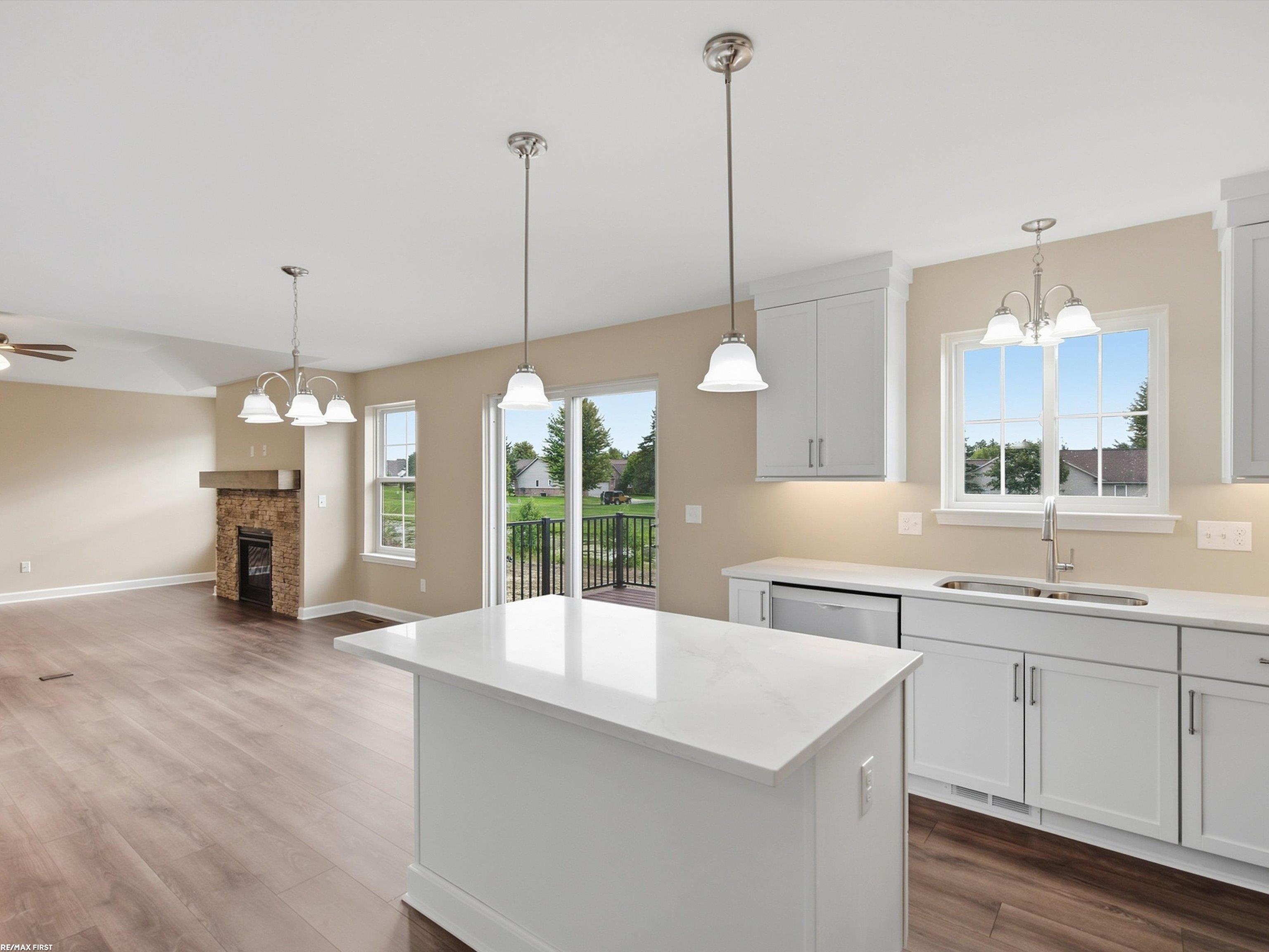Open-plan kitchen and living area with a large white island, stone fireplace, and sliding doors to a deck.