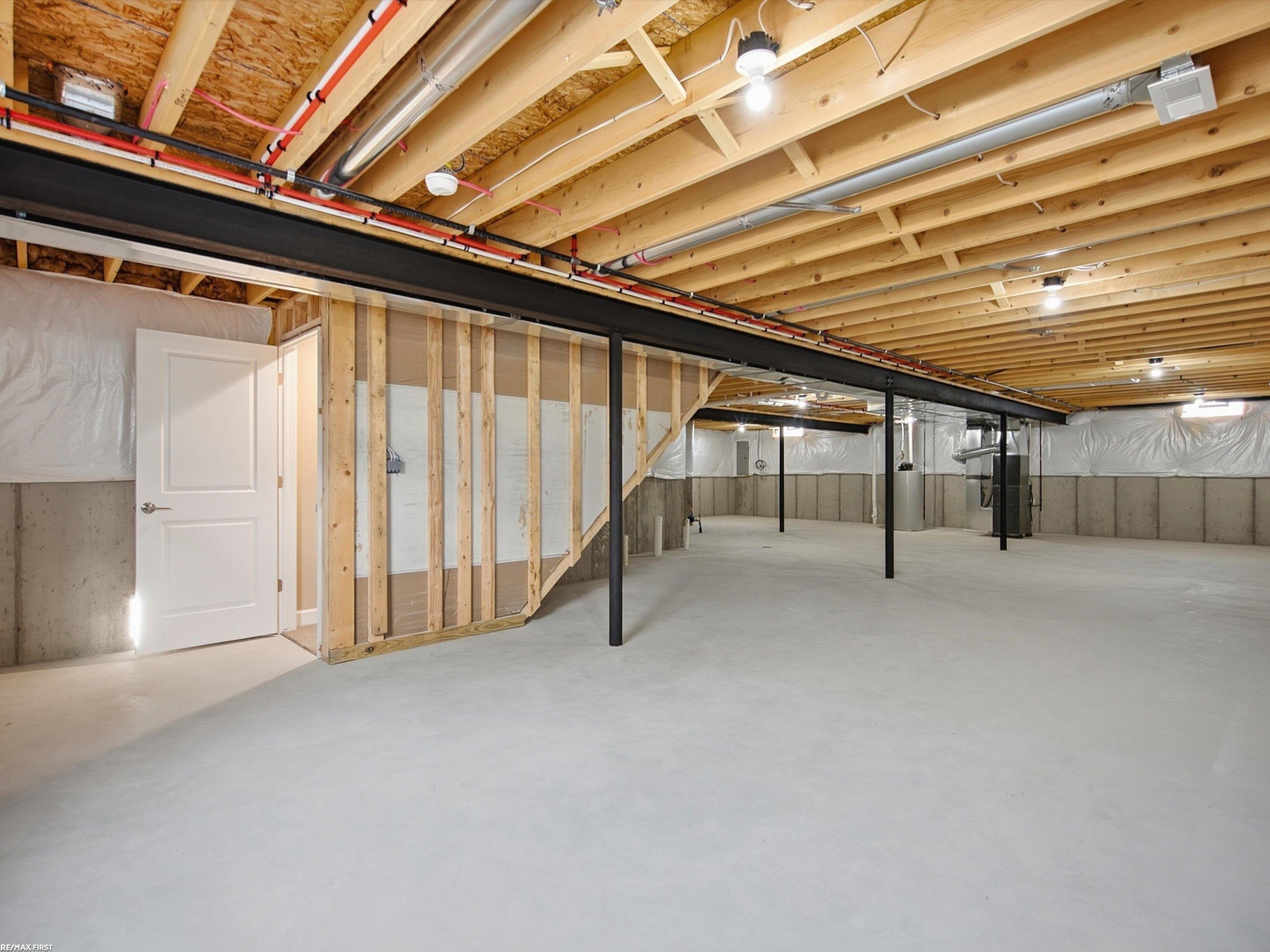 Unfinished basement with exposed ceiling joists, black support posts, and a wide concrete floor.