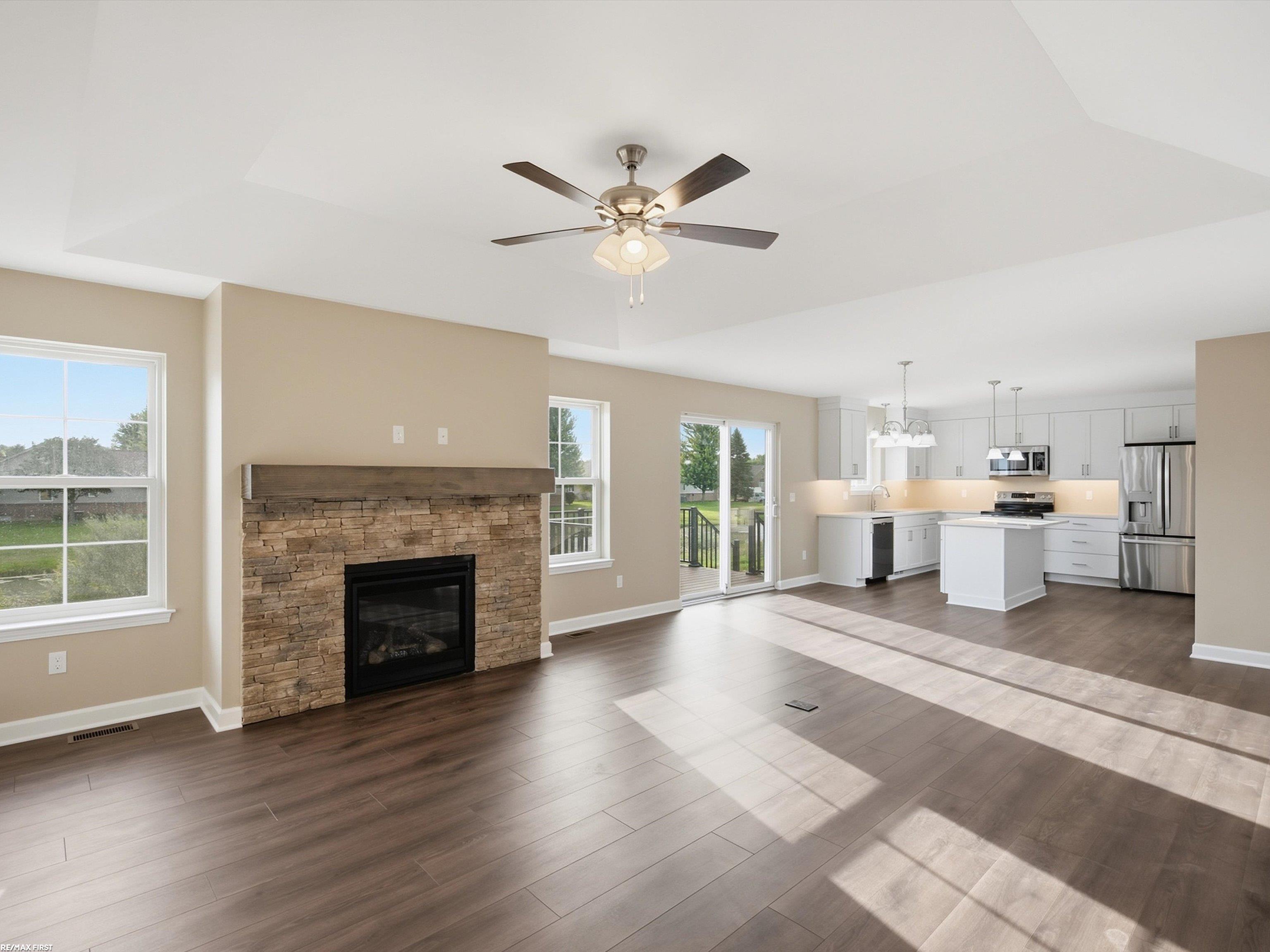 Open-plan living room and kitchen with a stone fireplace, white cabinets, and dark flooring.