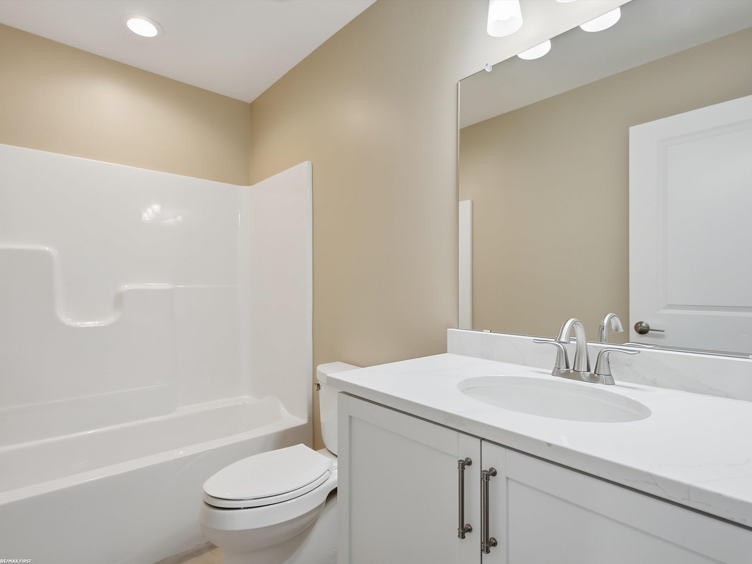 Bathroom with a white tub and shower, toilet, and vanity with an oval sink and chrome faucet.