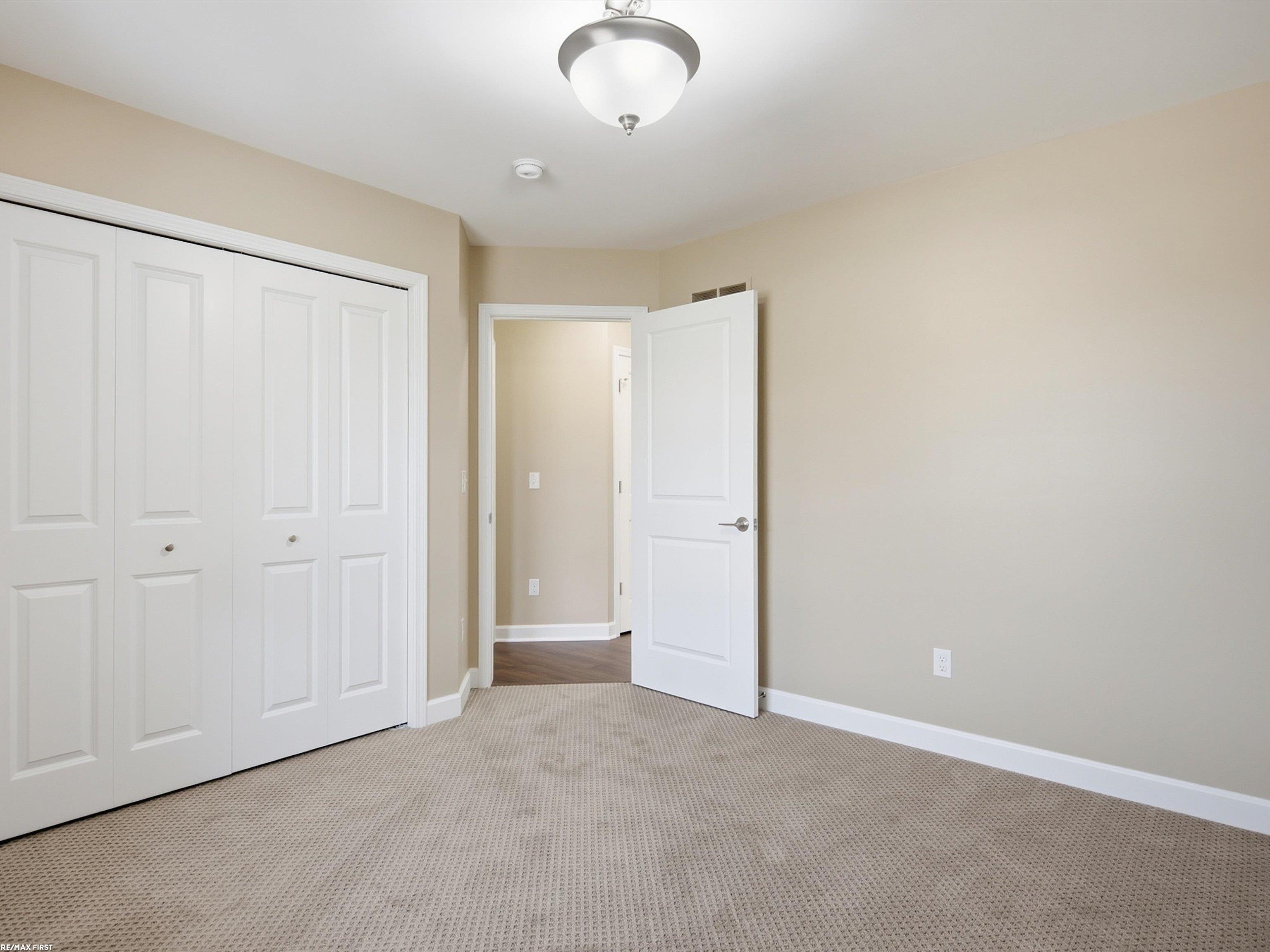 Empty bedroom with beige carpet, white paneled closet doors, and an open door to the hallway.