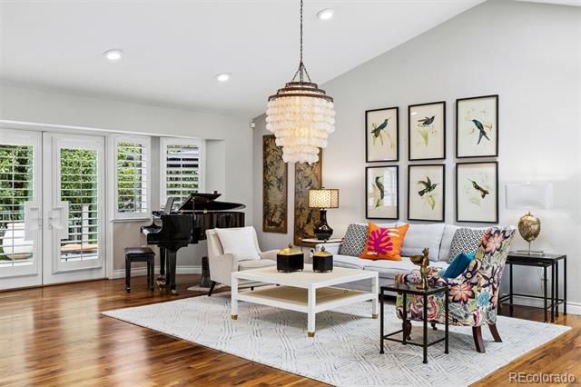 Living room with a black grand piano, white seating, crystal chandelier, and framed bird prints.