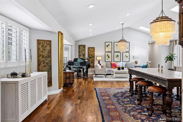 Open living and dining room with a grand piano, vaulted ceiling, hardwood floors, and long dining table.