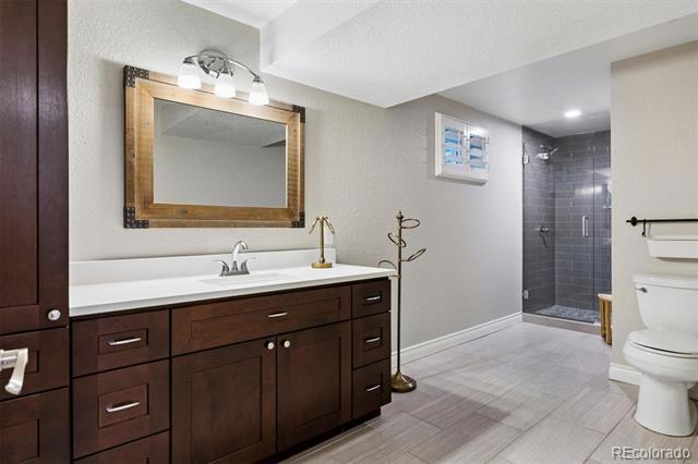Bathroom with dark wood vanity, framed mirror, gray tile walk-in shower, and white toilet.
