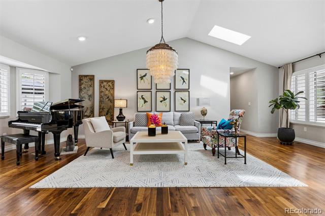 Living room with vaulted ceiling, hardwood floors, a piano, and a chandelier above the seating area.
