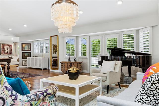 Living room with a black grand piano, plantation-shuttered windows, and colorful patterned chairs.