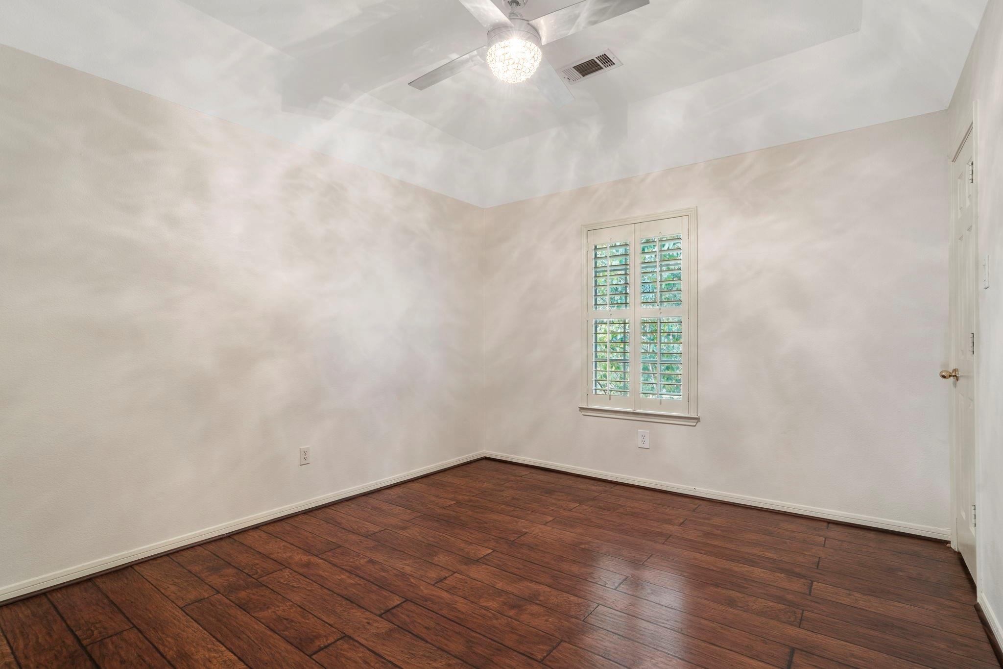 Empty bedroom with dark wood flooring, plantation shutters, and a ceiling fan.