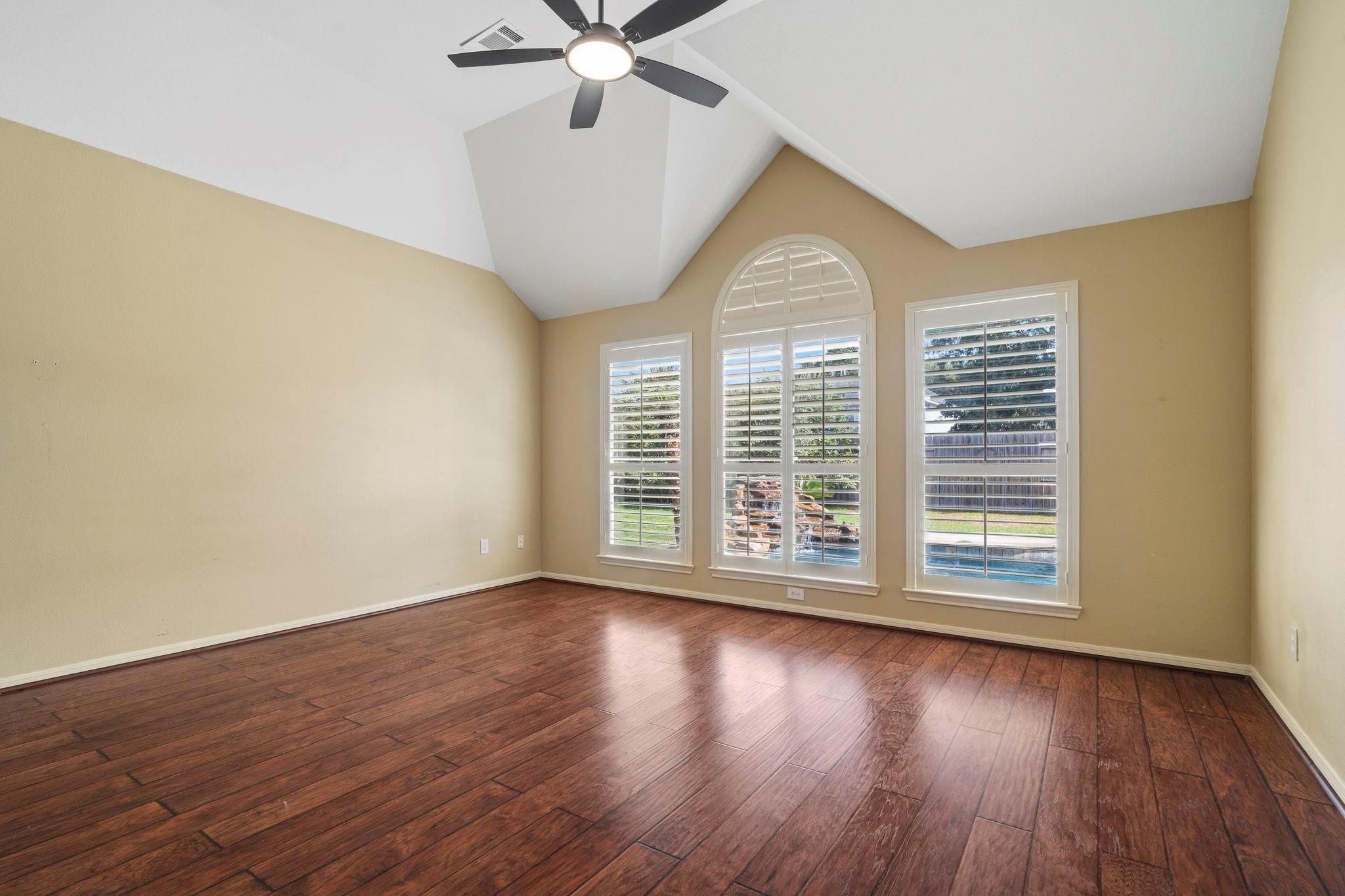 Empty room with vaulted ceiling, dark wood floors, and shuttered windows, including an arched window.