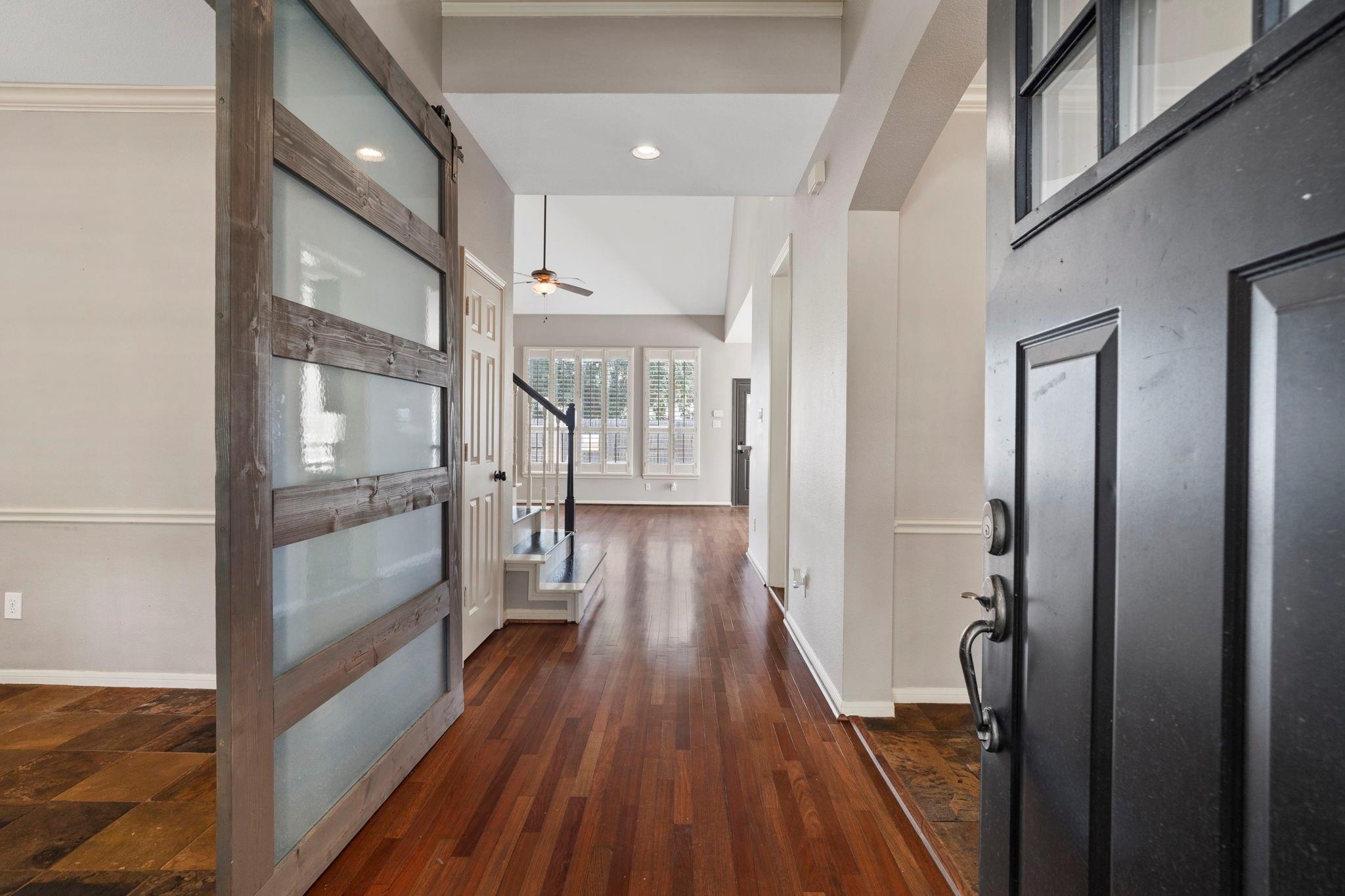 Entryway with hardwood floors, an open black front door, and a sliding frosted-glass barn door.