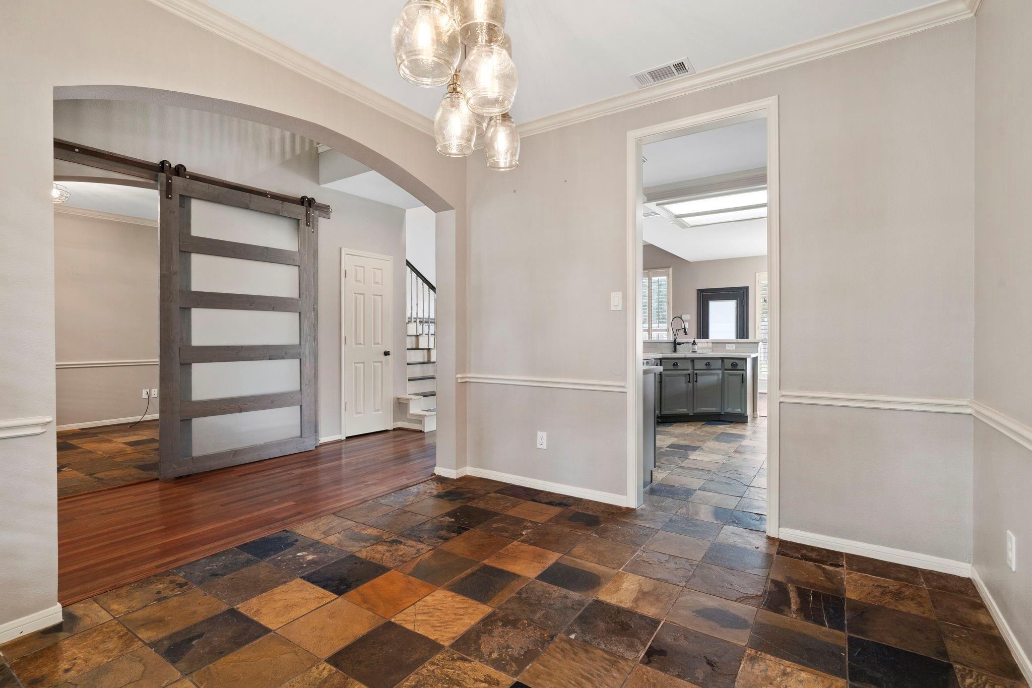 Foyer with multicolored slate tile floors, a dark barn door, and a view into the kitchen.