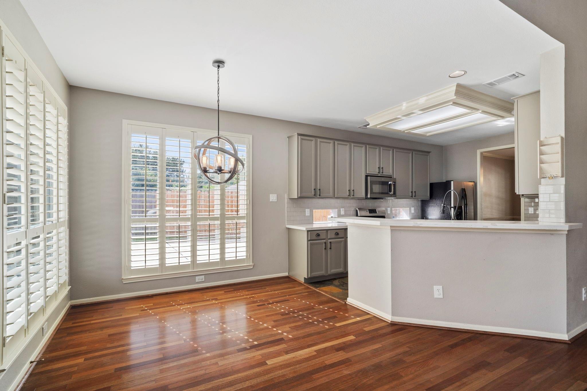 Open kitchen and dining area with a broad breakfast bar, gray cabinets, hardwood floors, and plantation shutters.