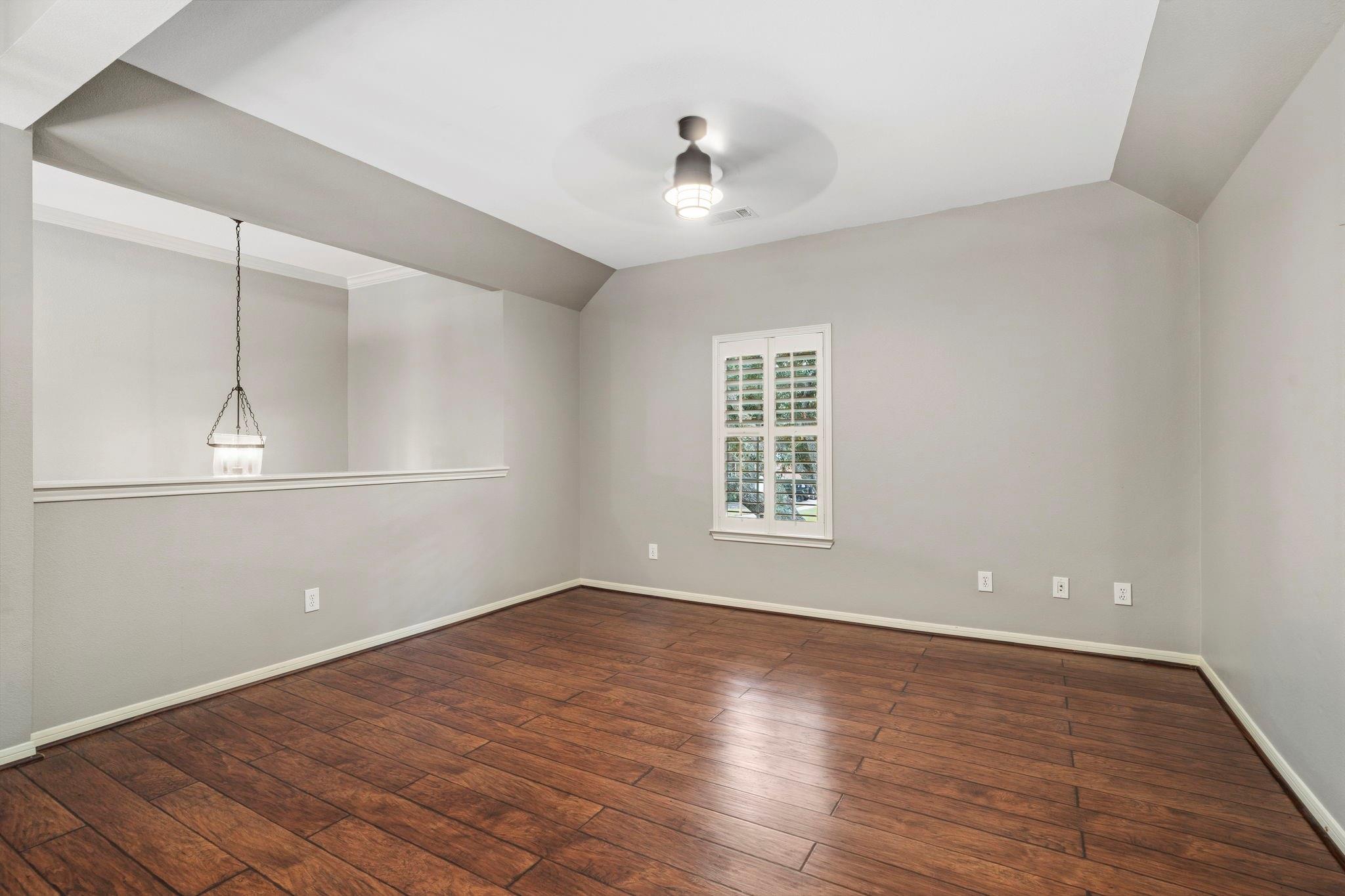Empty dining room with brown plank flooring, vaulted ceiling, and shuttered window.
