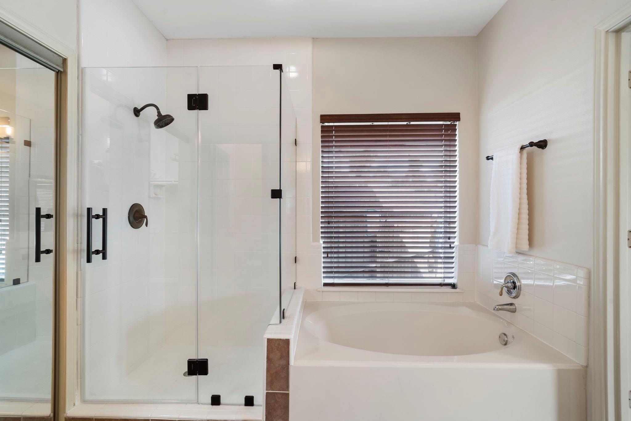 Bathroom with a glass shower, built-in soaking tub, and window with dark blinds.