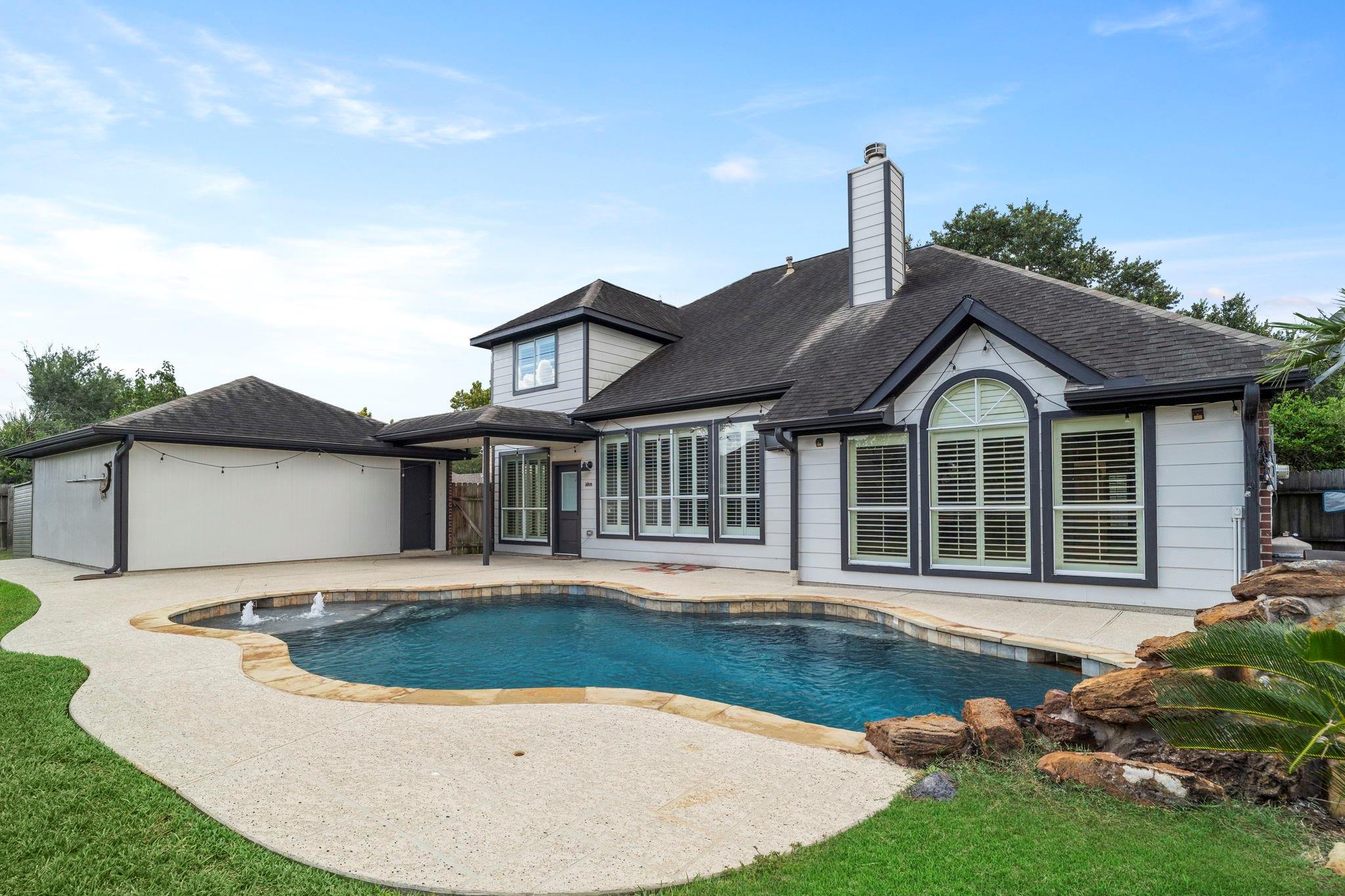 House rear with a curved swimming pool, two fountains, and a covered patio.