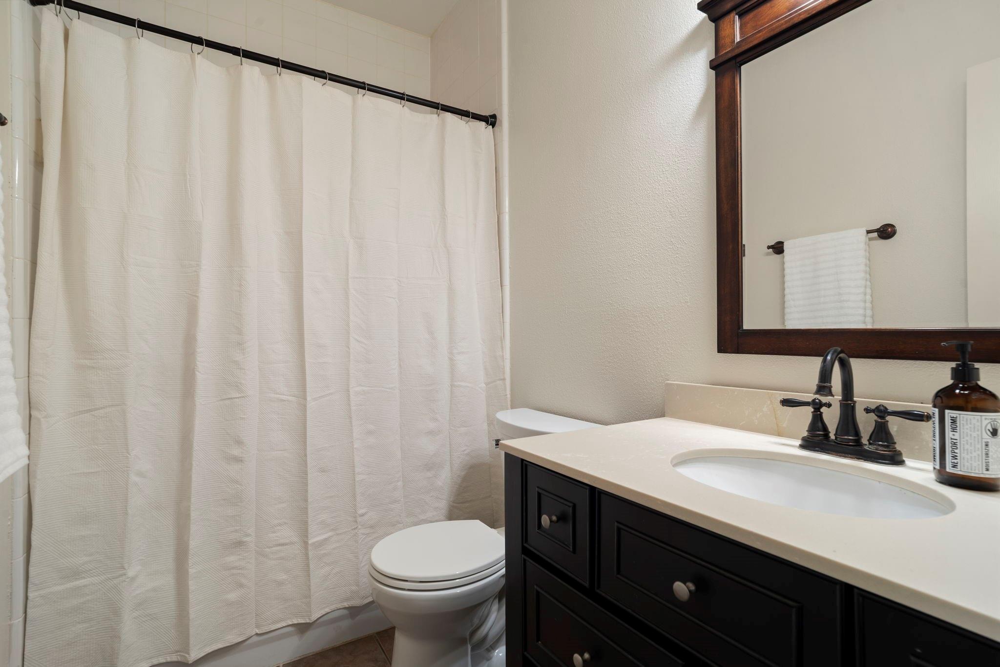 Bathroom with a white shower curtain, toilet, and dark wood vanity with an oval sink.